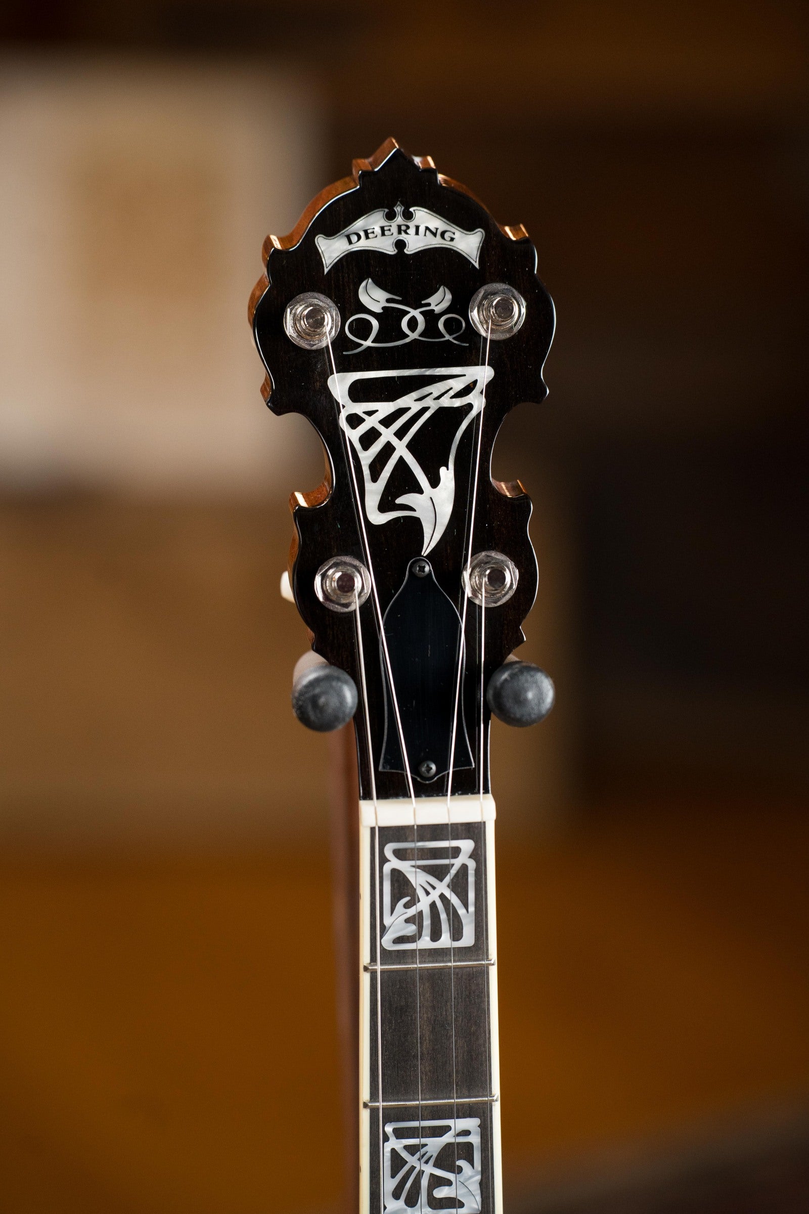 Close-up of a Deering Banjos Tony Trischka Silver Clipper Resonator Banjo (#0100) headstock with decorative inlays and the Deering logo, featuring spikes at frets 7, 8, 9, and 10—ideal for bluegrass musicians.