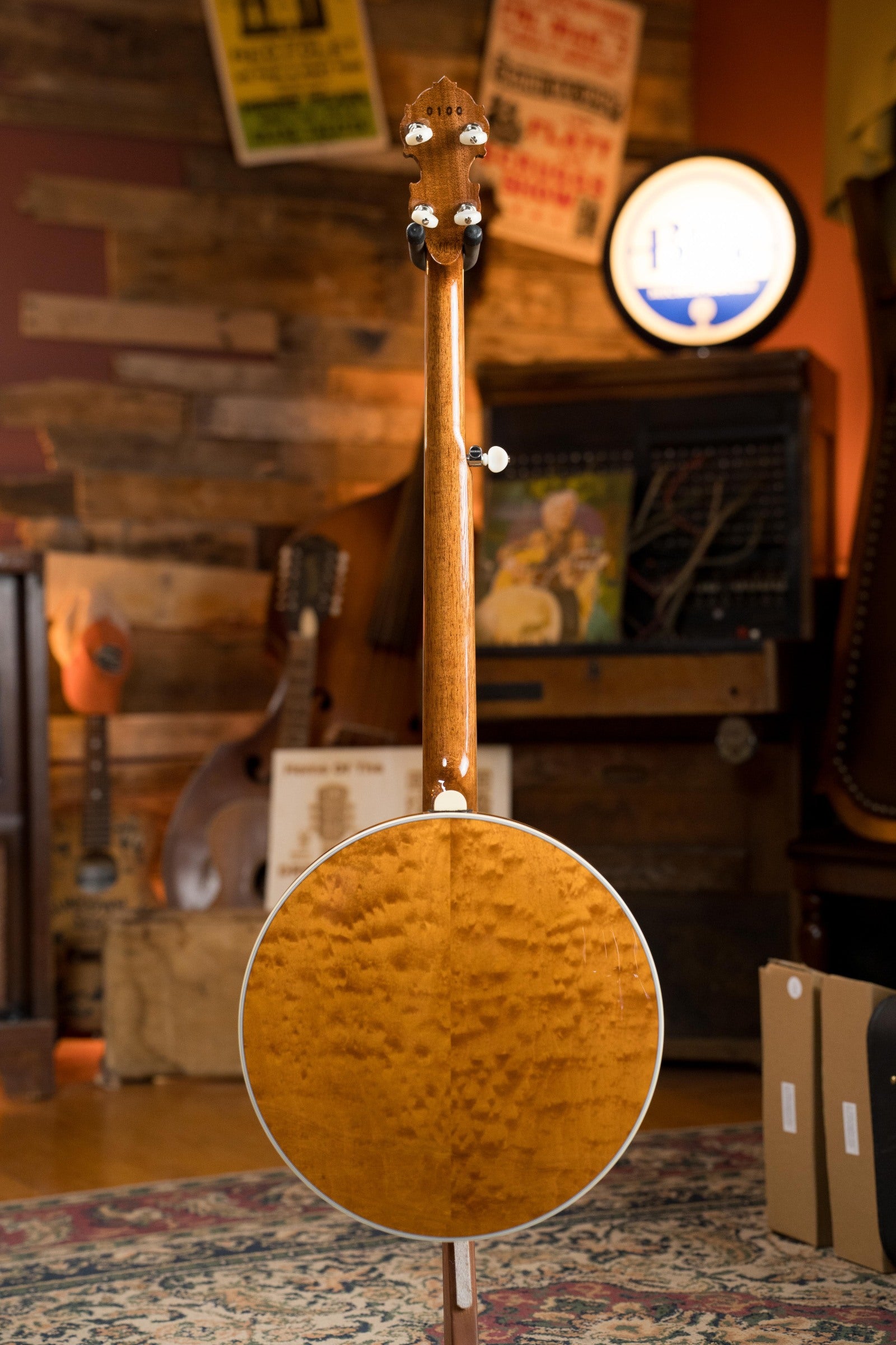A Deering Banjos Tony Trischka Silver Clipper Resonator Banjo w/Spikes Installed at 7, 8, 9, and 10 #0100 stands upright on a patterned rug in a cozy room with vintage posters, records, and bluegrass instruments.
