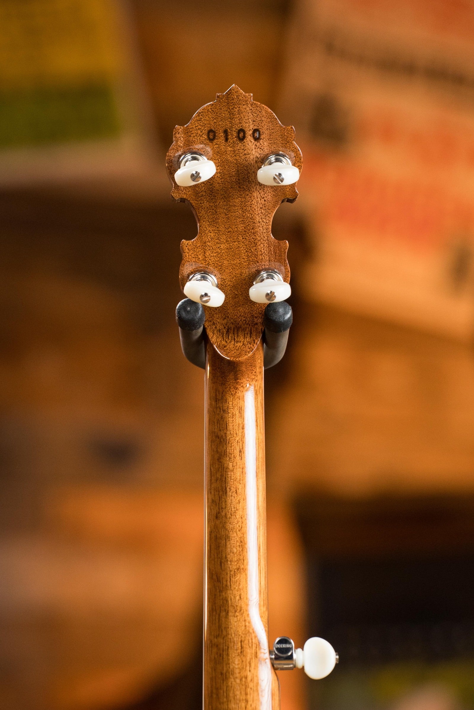 Close-up of the Deering Banjos Tony Trischka Silver Clipper Resonator Banjo w/Spikes Installed at 7, 8, 9, and 10 (#0100) headstock shows tuning pegs and serial number against a warm indoor background—ideal for bluegrass fans.