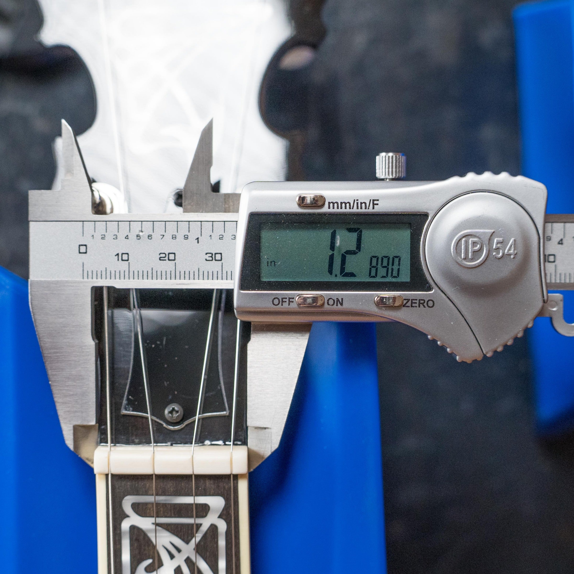 A digital caliper shows a guitar neck thickness of 12.89 mm near the first fret. Next to it sits a Deering Tony Trischka Silver Clipper Resonator Banjo w/Spikes Installed at 7, 8, 9, and 10—an ideal choice for bluegrass players.