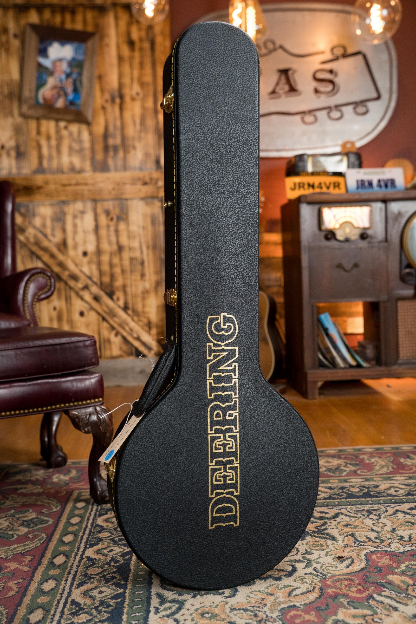 A Deering Banjos Tony Trischka Silver Clipper Resonator Banjo (#0100) with spikes at frets 7-10 is displayed upright on a patterned rug in a cozy room with wood paneling and vintage bluegrass decor.