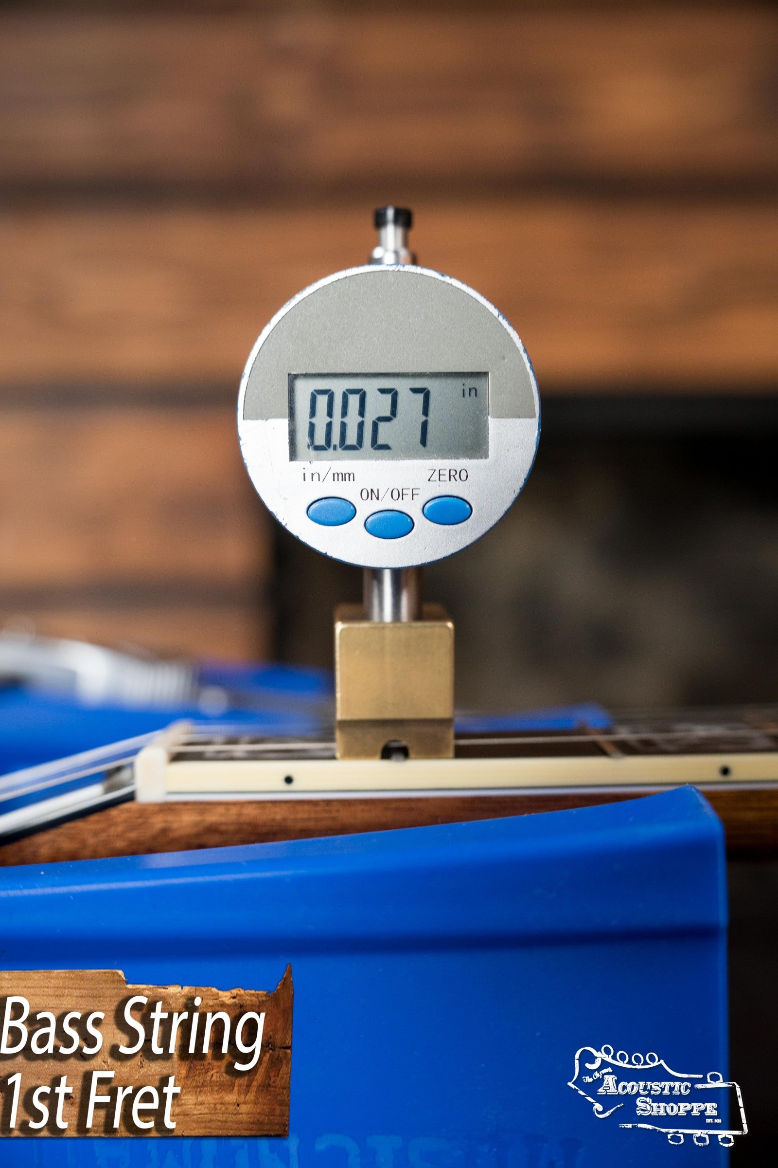 A digital gauge displays 0.027 inches for the bass string height at the 1st fret of a Deering Tony Trischka Silver Clipper Resonator Banjo w/Spikes by Deering Banjos—ideal for pro bluegrass or banjo setups from The Acoustic Shoppe.