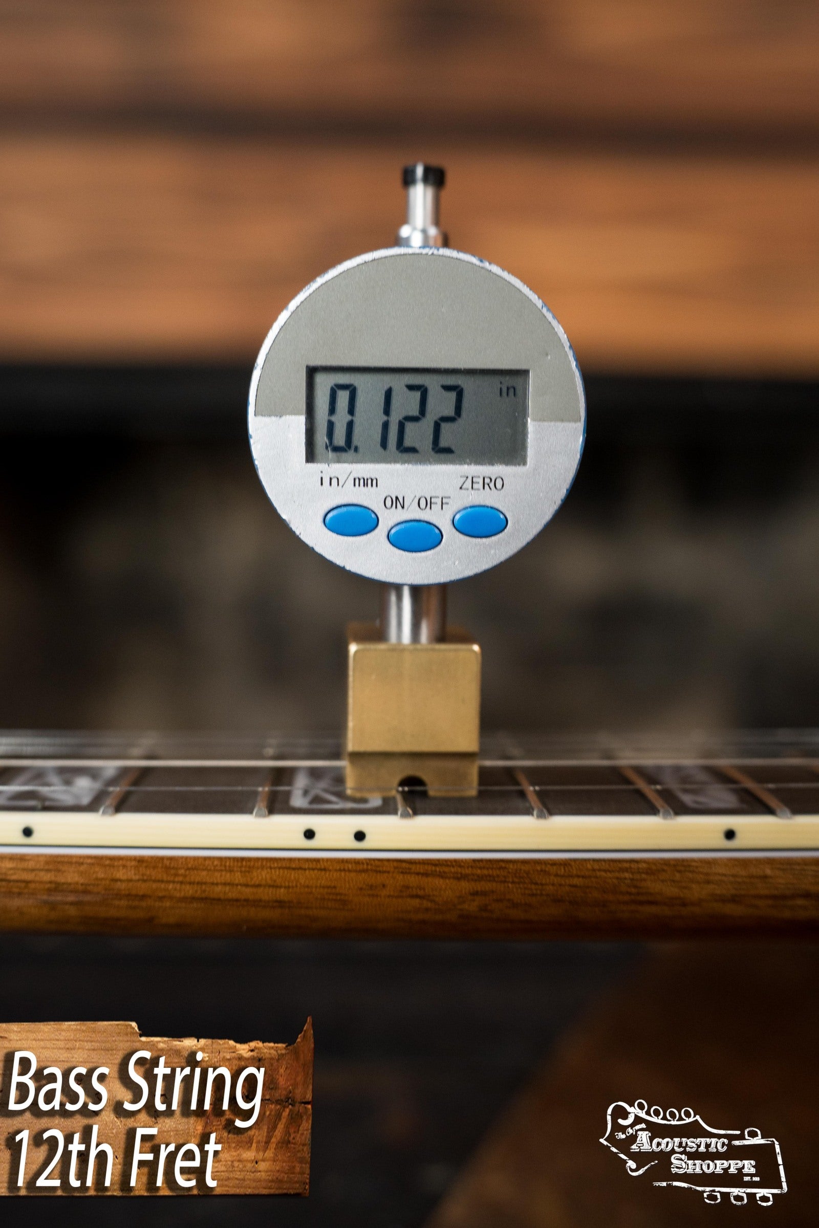 A digital gauge shows the bass string height at the 12th fret of a Deering Tony Trischka Silver Clipper Resonator Banjo w/Spikes (Deering Banjos) as 0.122 inches. Text reads Bass String 12th Fret and Acoustic Shoppe, trusted by bluegrass pros.