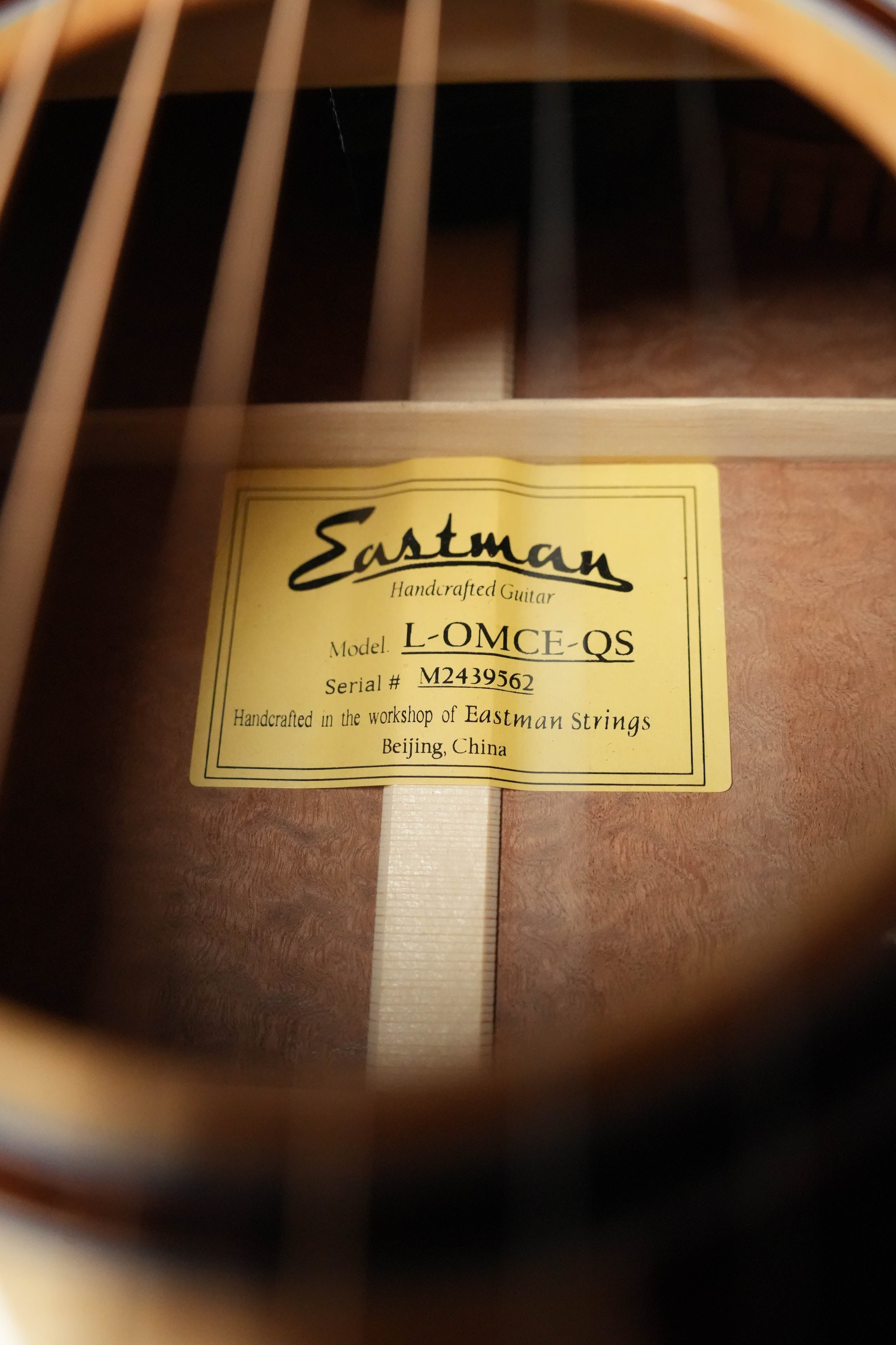 Close-up view through the sound hole of a *Dread-Not Certified Used* 2024 Eastman L-OMCE-QS Orchestra Model Acoustic-Electric Guitar, showing a label: Handcrafted in the workshop of Eastman Guitars, Beijing, China.