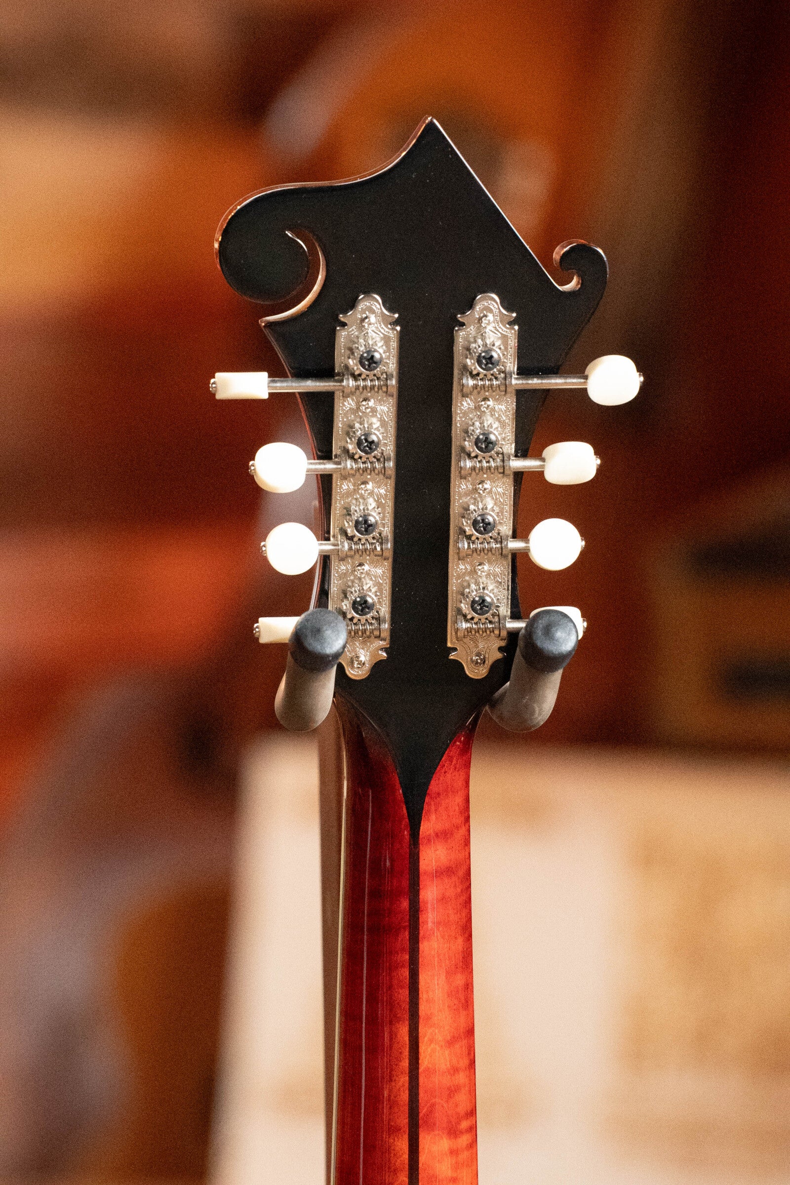Close-up of the back headstock on a *Dread-Not Certified Used* Eastman MDA815 F-Style Mandola Classic Finish #4978 by Eastman Guitars, showing ornate tuning pegs and a rich reddish wood tone against a blurred background.