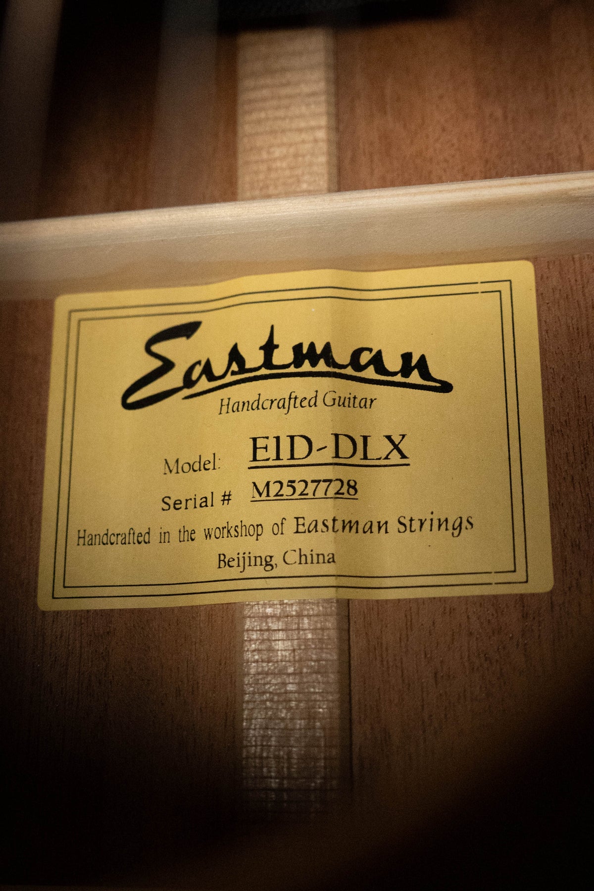 A close-up of a yellow label inside an Eastman Guitars E1D-DLX Sitka/Sapele Dreadnought w/Fishman Pickup #7728, reading: Handcrafted in the workshop of Eastman Strings, Beijing, China.