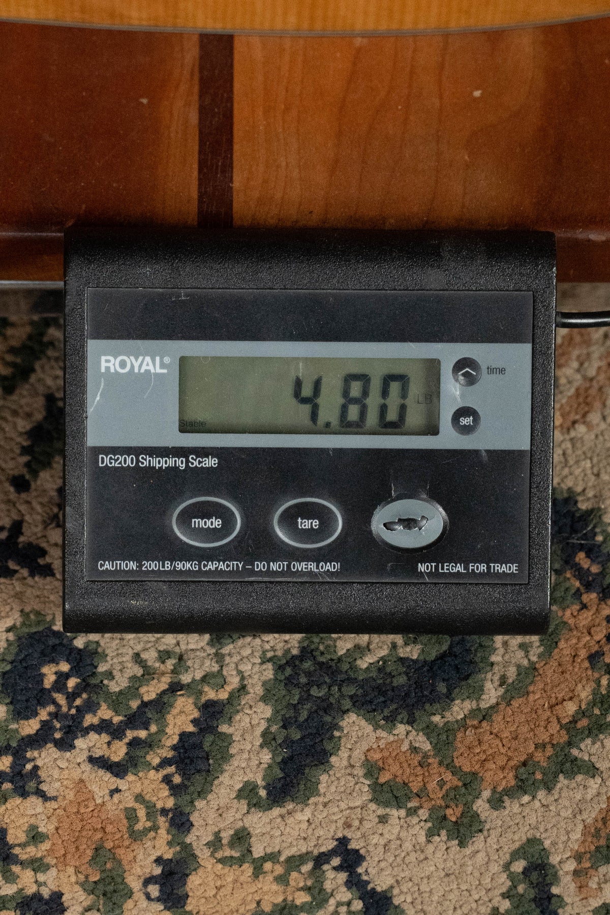 A digital shipping scale (ROYAL DG200) on a patterned carpet shows 4.80 lbs, with part of an Eastman Guitars E1D-DLX Sitka/Sapele Dreadnought Guitar w/Fishman Pickup (#7728) visible above it.