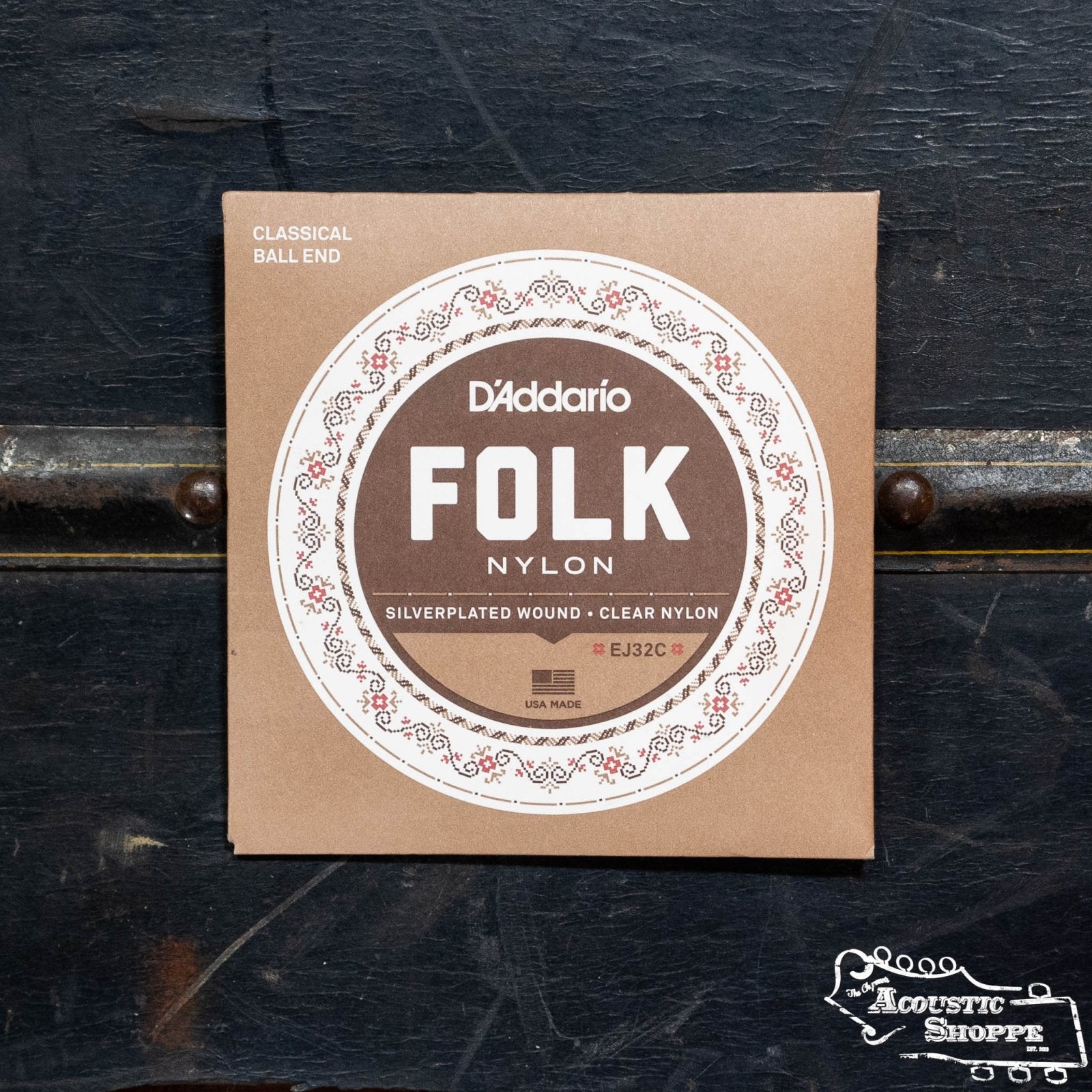 A D'Addario EJ32C Set Folk Nylon Silver Wound/Ball End Clear Trebles from The Acoustic Shoppe rests on a black surface, featuring decorative white and brown circular packaging.