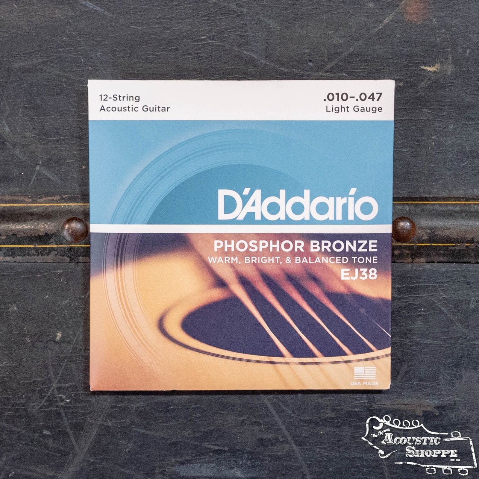 A pack of DAddario EJ38 12-String Phosphor Bronze Acoustic Guitar Strings Light 10-47 sits on a dark surface, displaying the DAddario brand and a guitar image, with details highlighting warm, bright, and balanced tone.