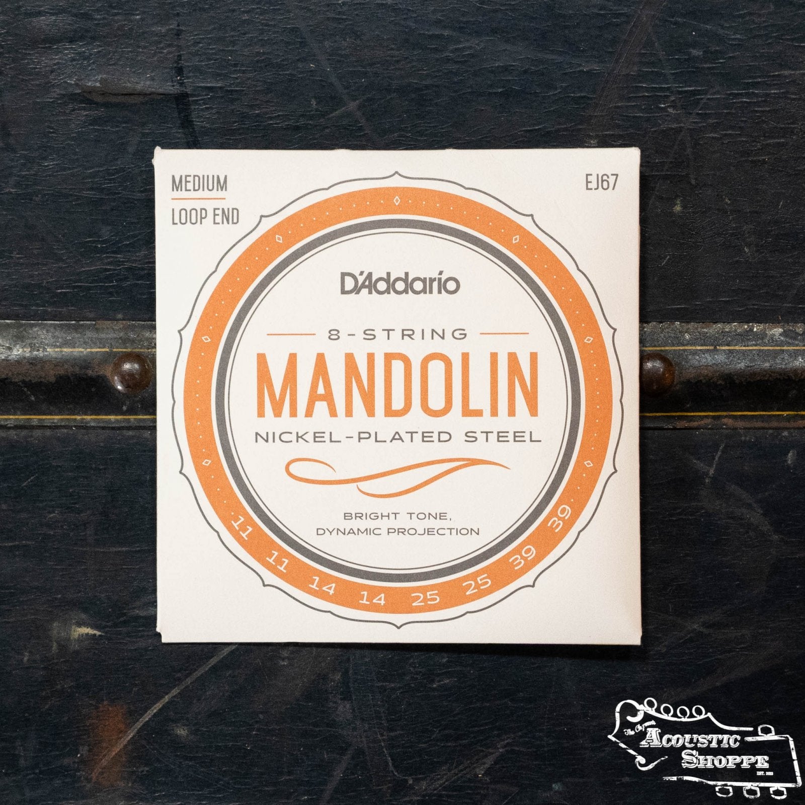 A pack of D'Addario EJ67 Set Mandolin Nickel Medium 11-39 strings, shown on a dark wooden surface with The Acoustic Shoppe logo in the bottom right—ideal for your acoustic mandolin.