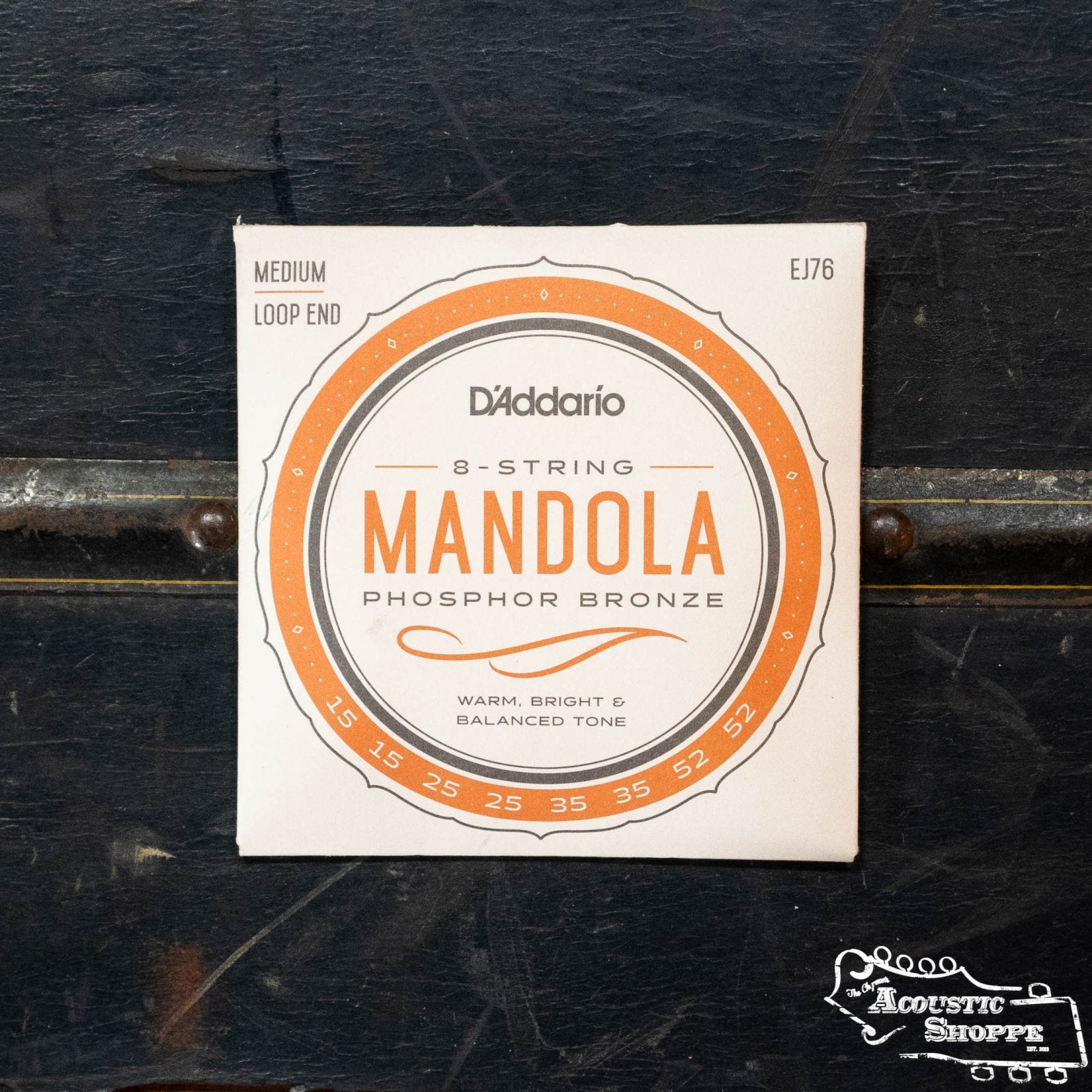 A pack of D'Addario EJ76 Mandola Phosphor Bronze Medium 15-52 strings sits on a dark surface. The packaging showcases a warm, bright, balanced tone and displays The Acoustic Shoppe logo in the bottom right corner.
