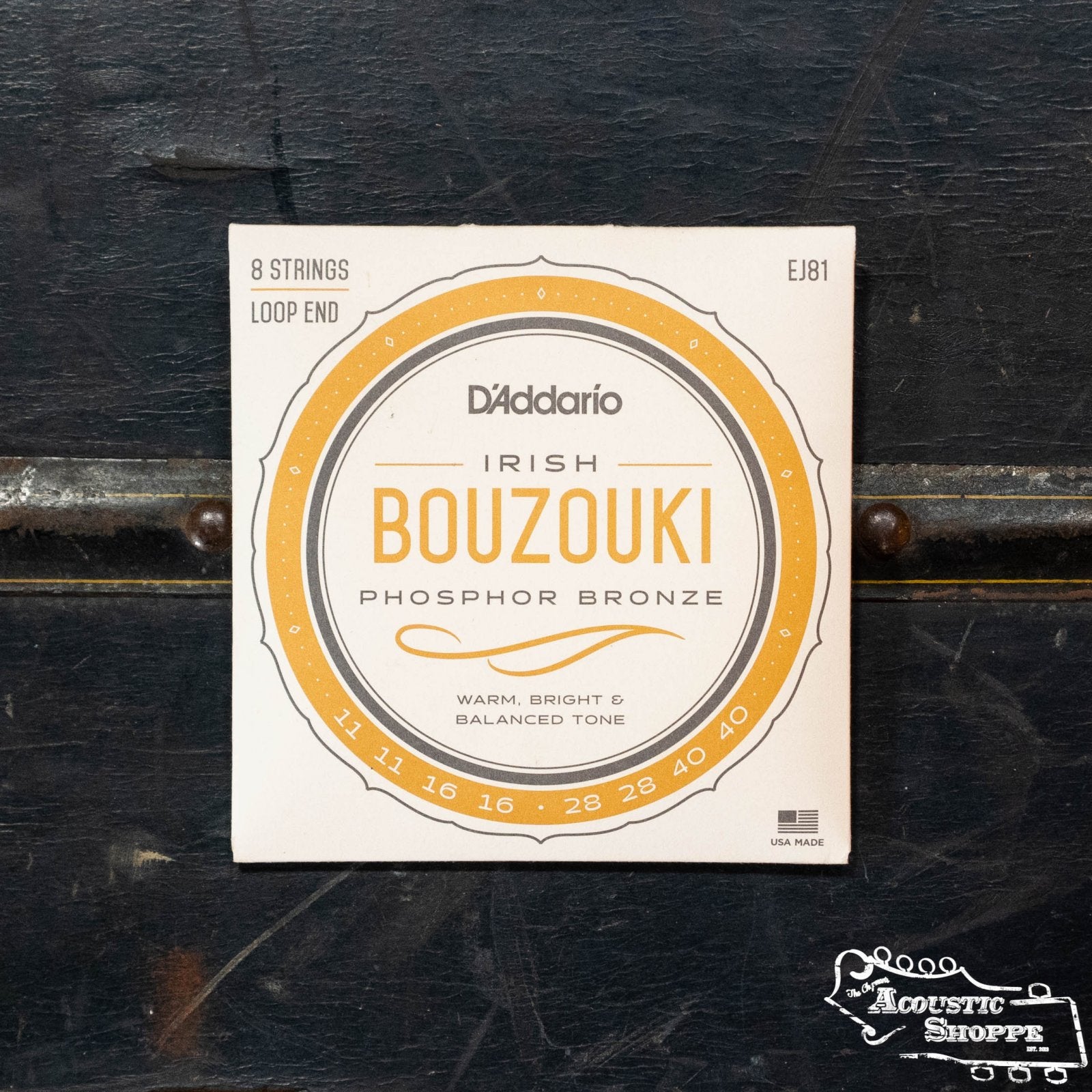 A pack of D'Addario EJ81 Irish Bouzouki Strings (8 phosphor bronze, gauges 11-16-28-40, loop end) by D'Addario rests on dark wood. The packaging notes a warm, bright, balanced tone.