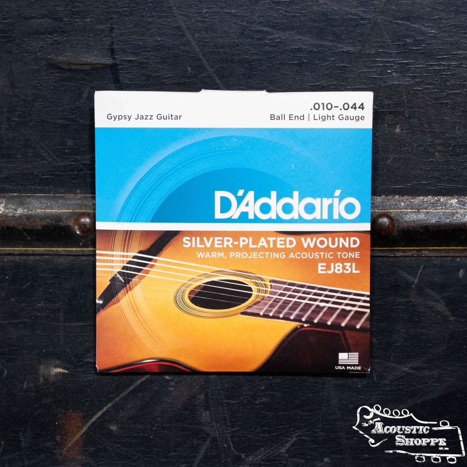 A pack of DAddario EJ83L Gypsy Jazz Ball End Acoustic Guitar Strings Light 10-44 rests on a dark surface, with packaging that displays part of an acoustic guitar.