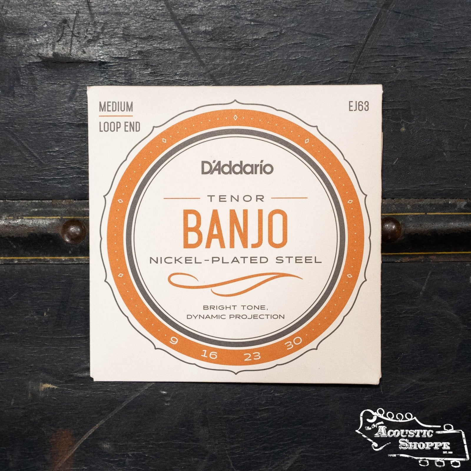 A DAddario EJ63 Nickel 4-String Tenor Banjo 9-23 pack sits on a dark surface, labeled Nickel-Plated Steel, Bright Tone, Dynamic Projection, Medium, Loop End, ideal for C-G-D-A tuning. The Acoustic Shoppe logo appears in the bottom right corner.