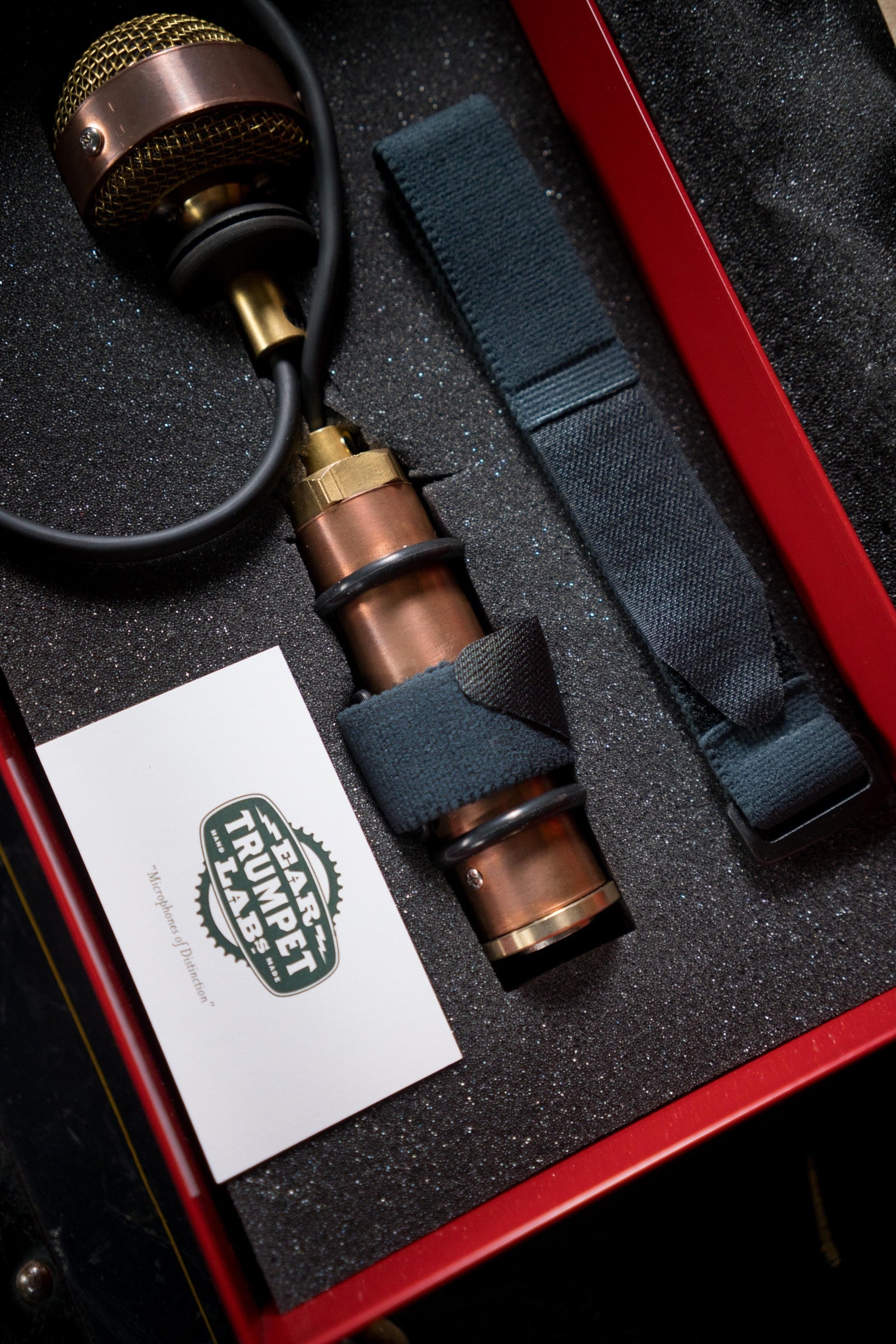The Ear Trumpet Labs Nadine Upright Bass Microphone, a vintage-style copper mic with gold mesh head, is secured in foam inside a red case with a fabric strap and Ear Trumpet Labs card—renowned for its natural sound.