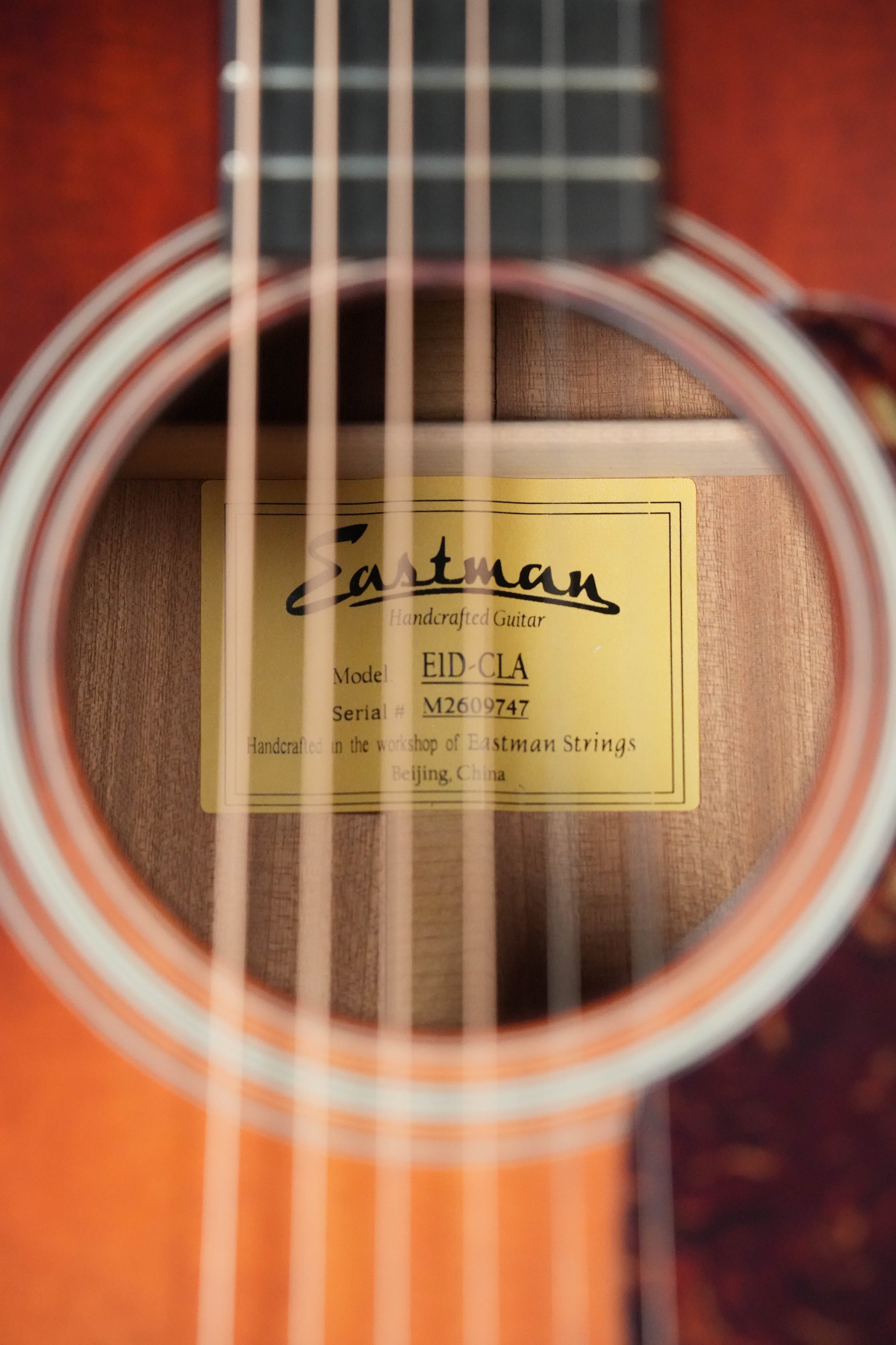 Close-up through the strings of an Eastman Guitars E1D-CLA Classic Finish Dreadnought Acoustic Guitar #9747, highlighting its solid Sitka spruce top and label inside. Made in Beijing, China.