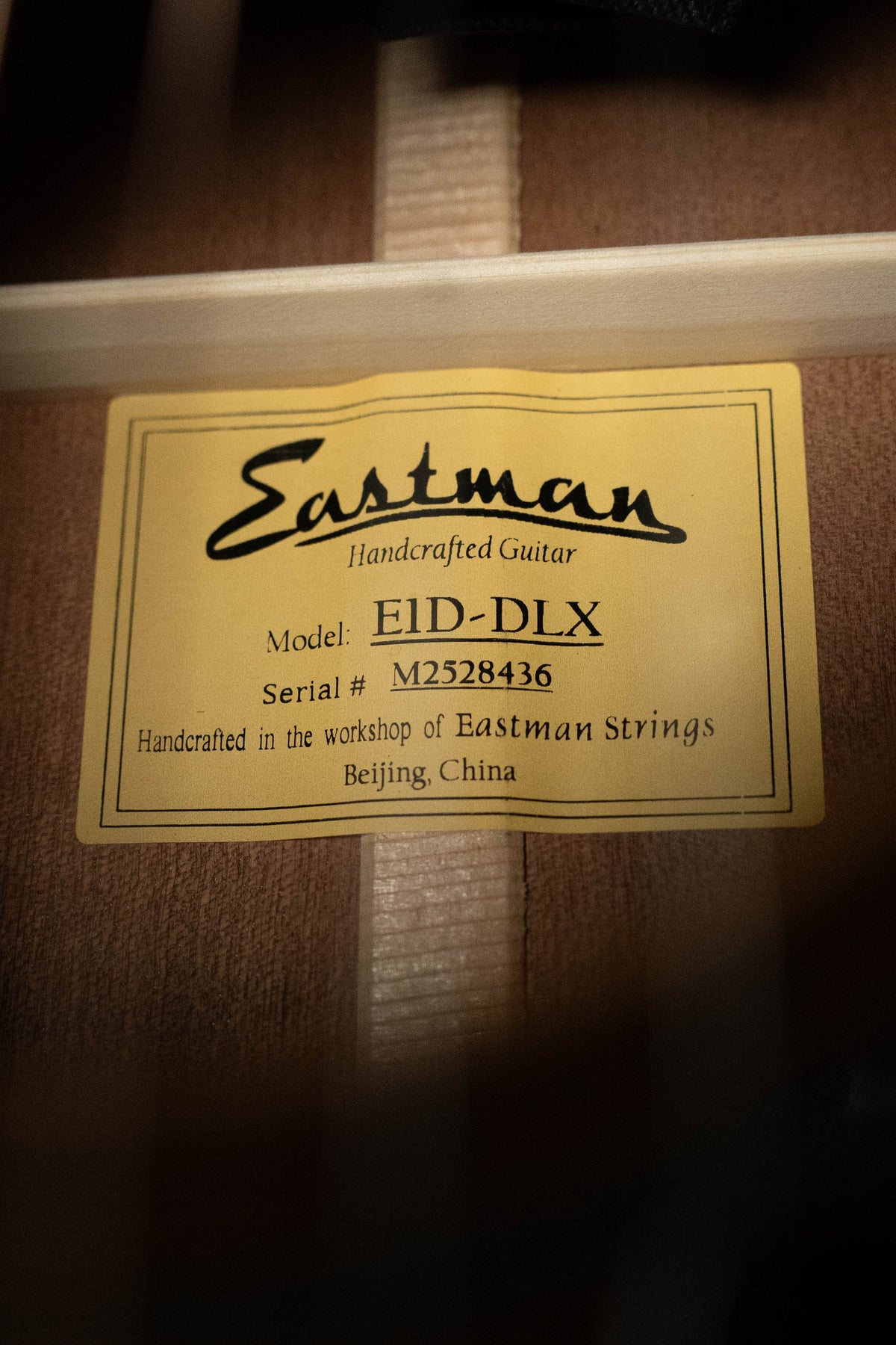 A yellow label inside the wooden dreadnought reads: Eastman Guitars Handcrafted Guitar, Model: E1D-DLX Sitka/Sapele w/Fishman Pickup #8436, made in the workshop of Eastman Guitars, Beijing, China.
