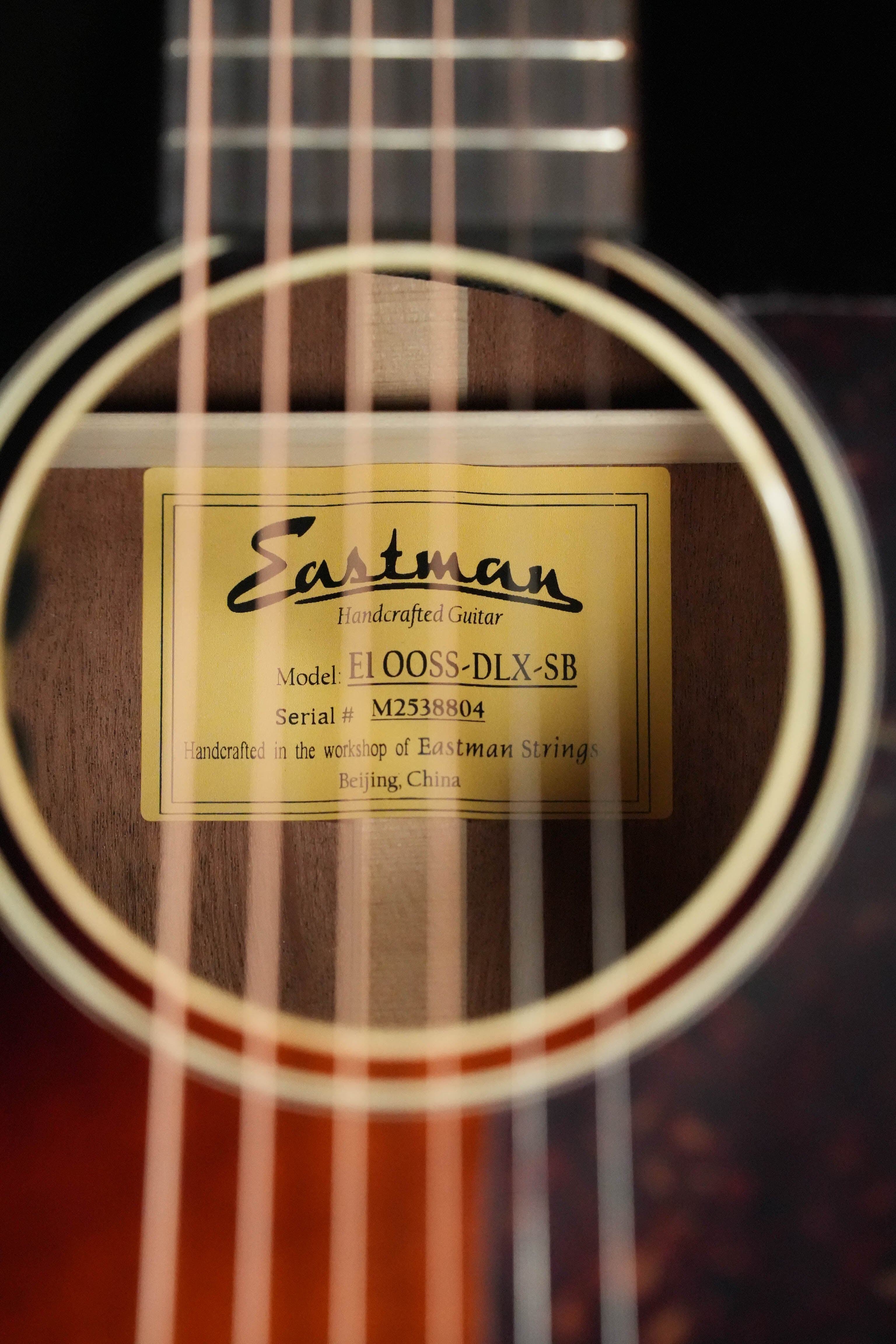 Close-up of an Eastman Guitars E1OOSS-DLX-SB Sunburst 00 Acoustic-Electric Guitar (#8804) soundhole, with its inside label visible and strings in the foreground.
