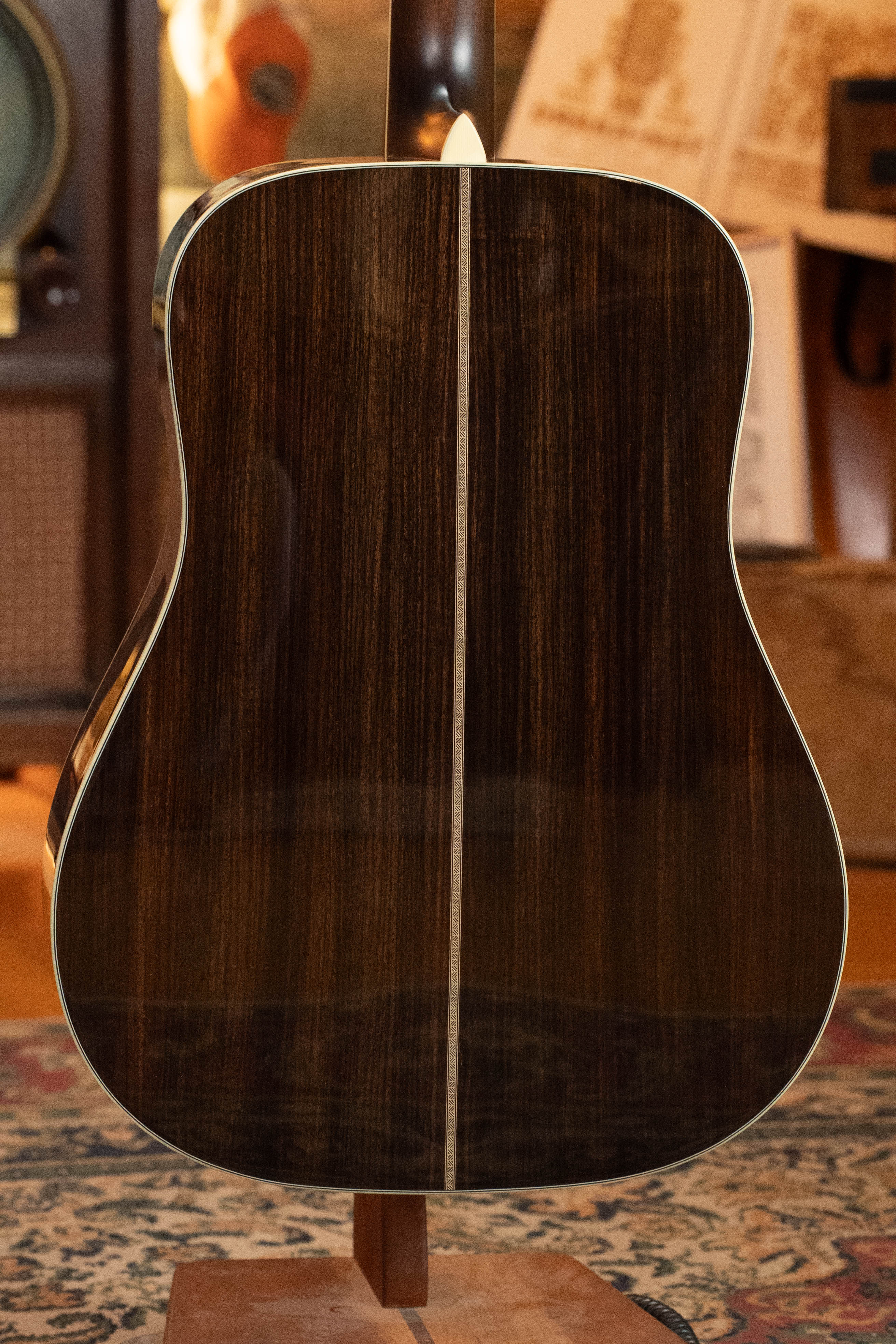 The image shows the back of an Eastman Guitars E20D-LSH-TC Thermo-Cured Adirondack/Rosewood Large Soundhole Dreadnought Acoustic Guitar #3917 with a dark wood finish, light center stripe, and white binding, displayed upright on a stand indoors.
