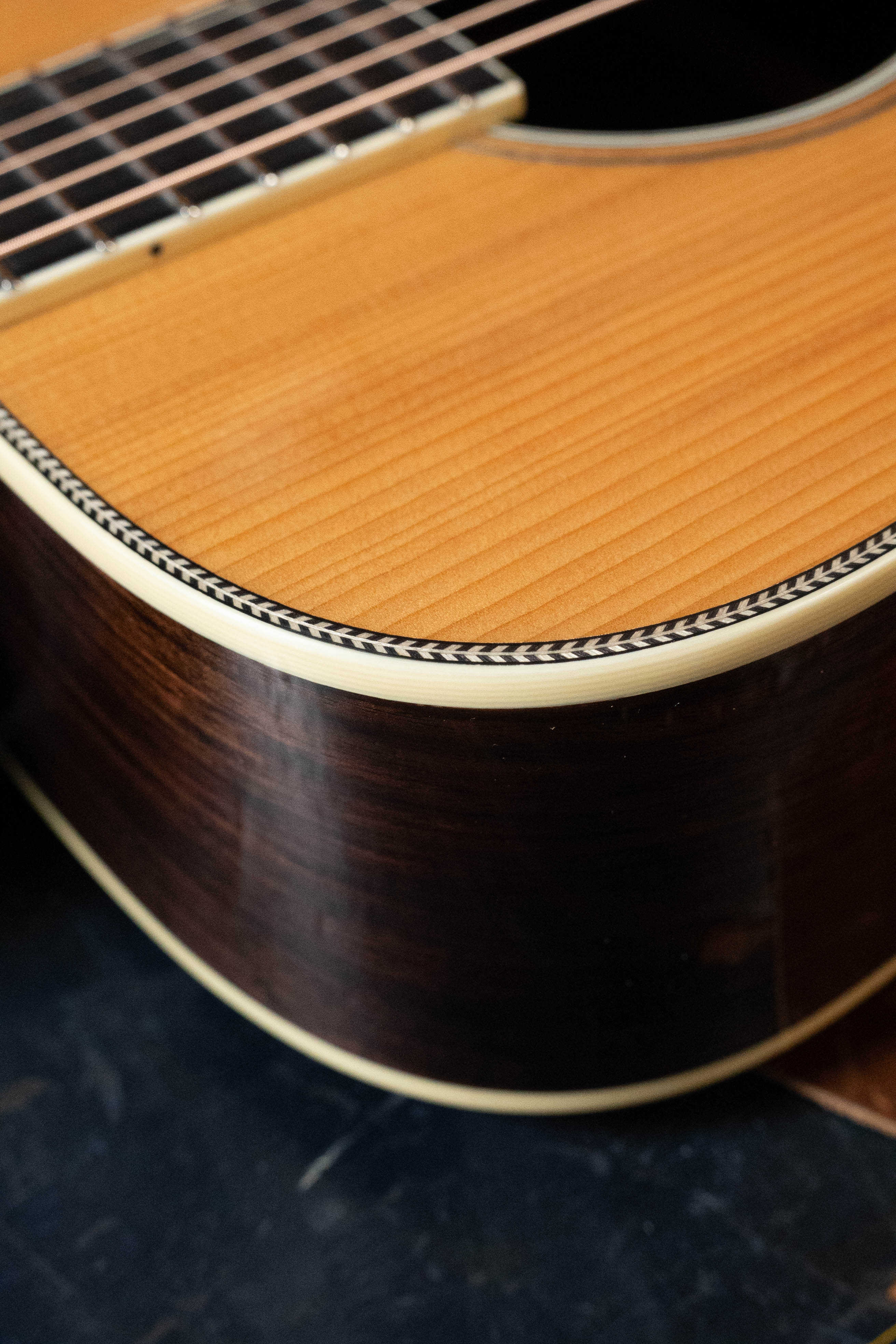 Close-up of an Eastman Guitars E20D-LSH-TC #3917 dreadnought, highlighting its thermo-cured Adirondack spruce top, rosewood sides, decorative binding, and part of the fretboard with metal strings.
