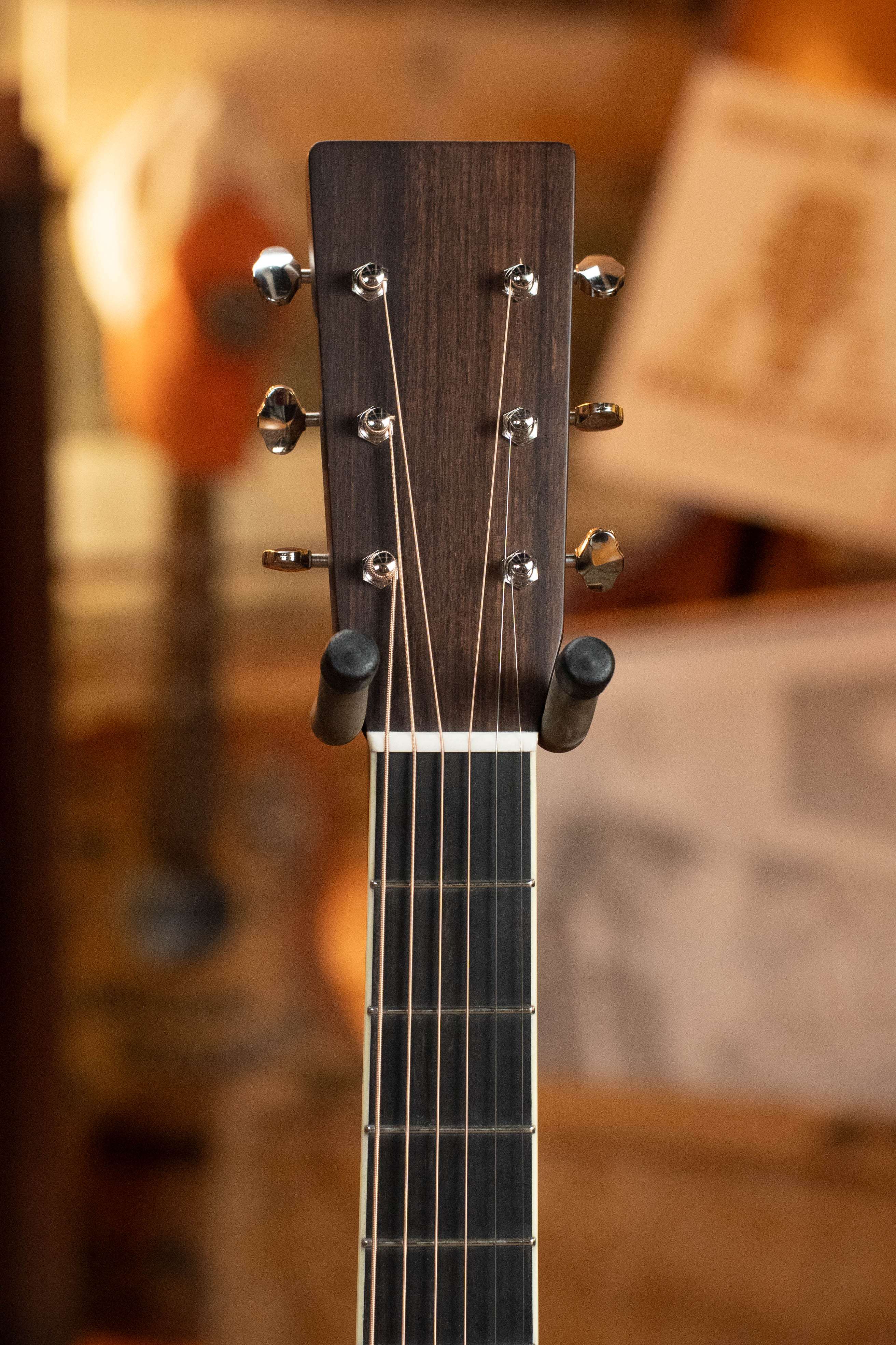 Close-up of the Eastman Guitars E20D-LSH-TC Thermo-Cured Adirondack/Rosewood Large Soundhole Dreadnought Acoustic Guitar #3917 headstock, showing tuning pegs and strings against a blurred, warm-colored background.