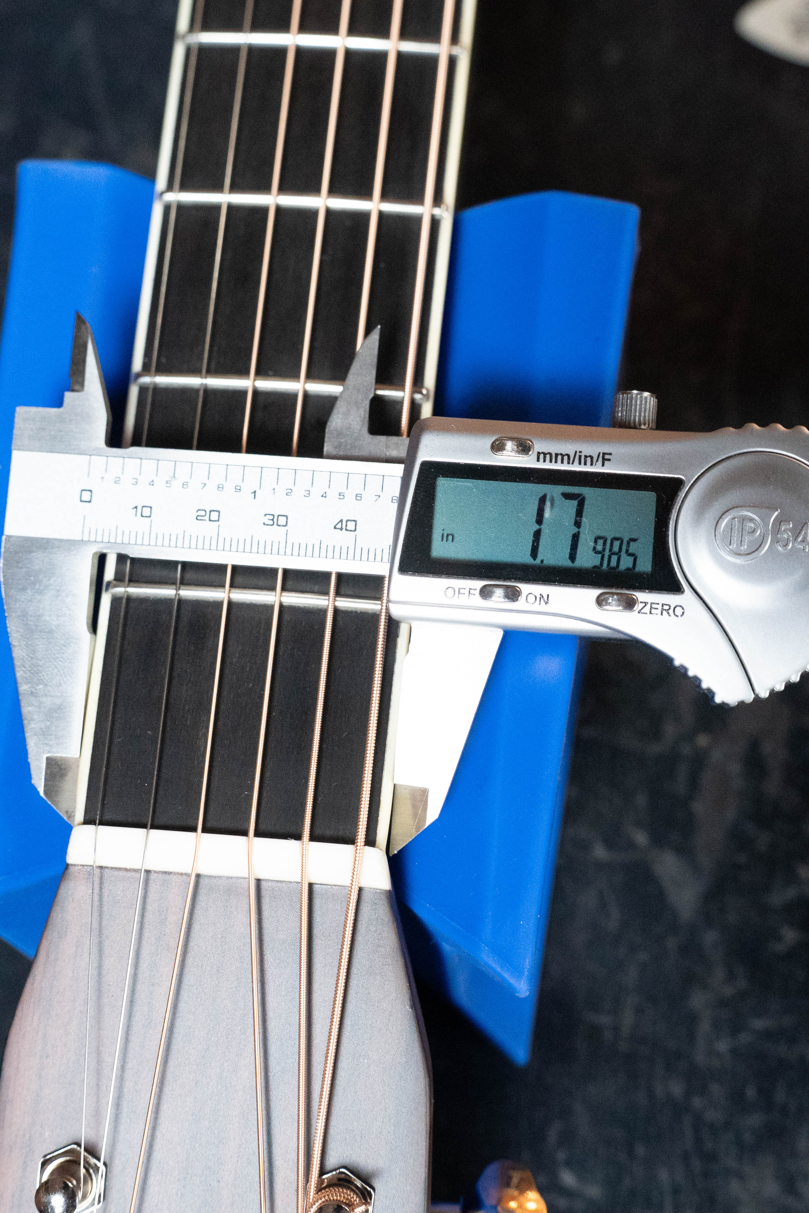A digital caliper shows the Eastman Guitars E20D-LSH-TC neck width near the nut as 41.98 mm, with its thermo-cured Adirondack spruce top and strings in view, supported by a blue holder above the fretboard.