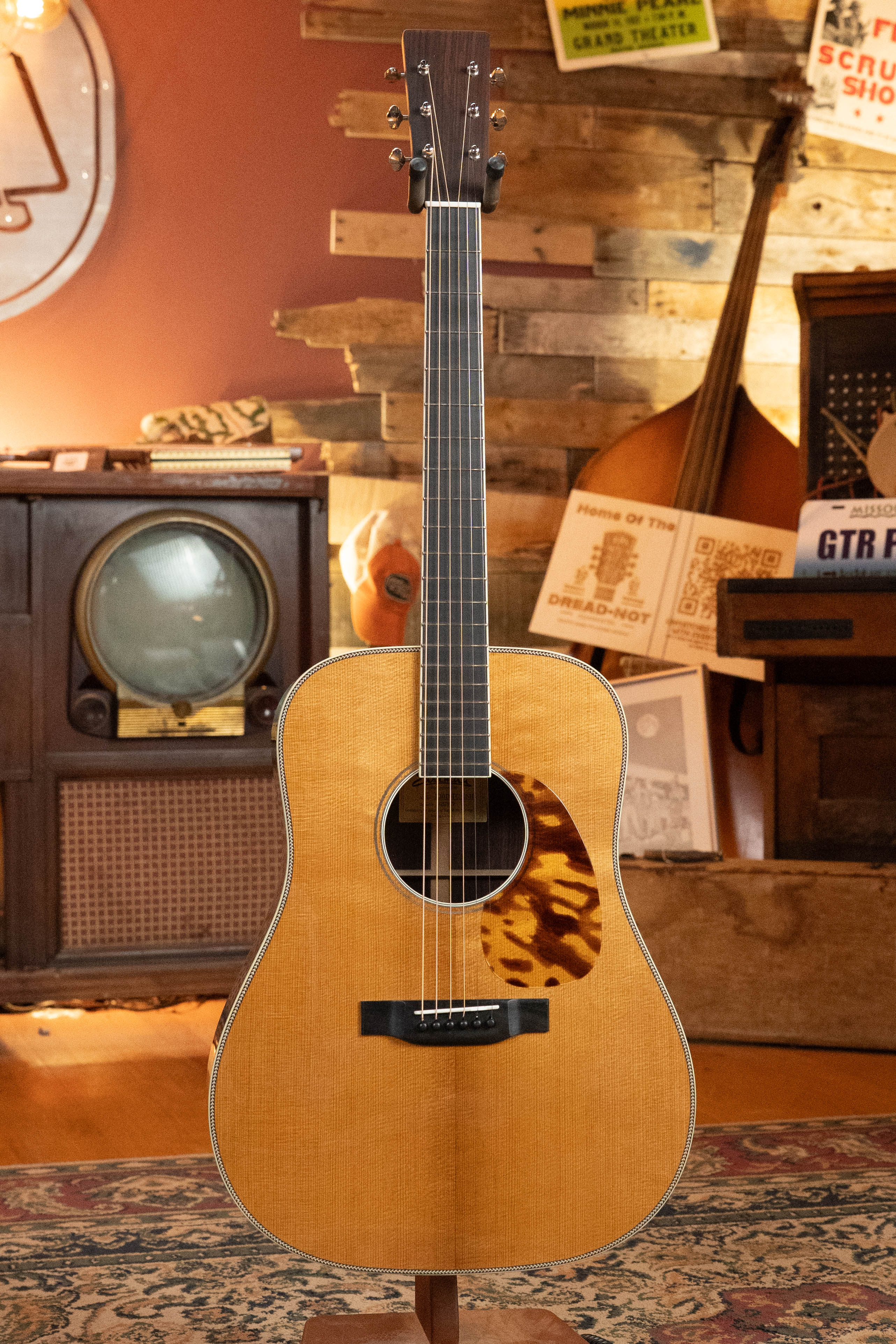 An Eastman Guitars E20D-LSH-TC Thermo-Cured Adirondack/Rosewood Large Soundhole Dreadnought Acoustic Guitar #8072 stands upright in a cozy, vintage-style room with a retro TV and wooden decor in the background.