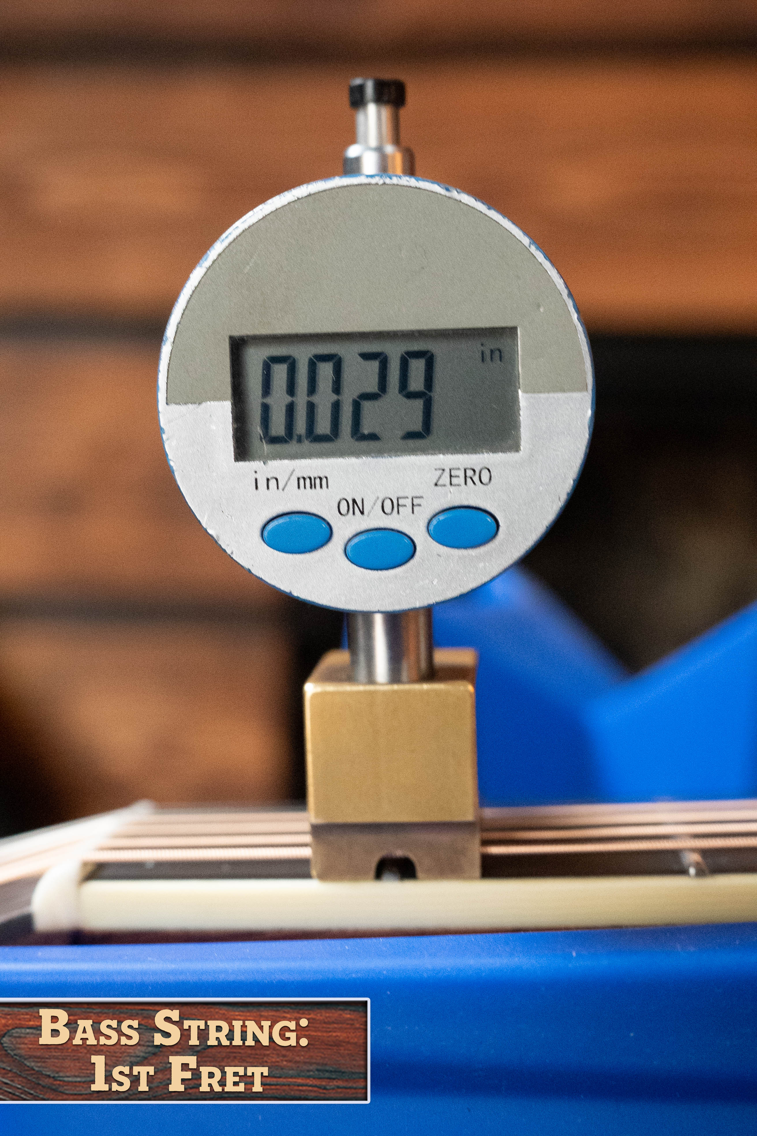 A digital caliper measures 0.029 inches at the 1st fret of a bass guitar string, echoing the precise setup found on the Eastman Guitars E20D-LSH-TC Thermo-Cured Adirondack/Rosewood Large Soundhole Dreadnought Acoustic Guitar #8072.