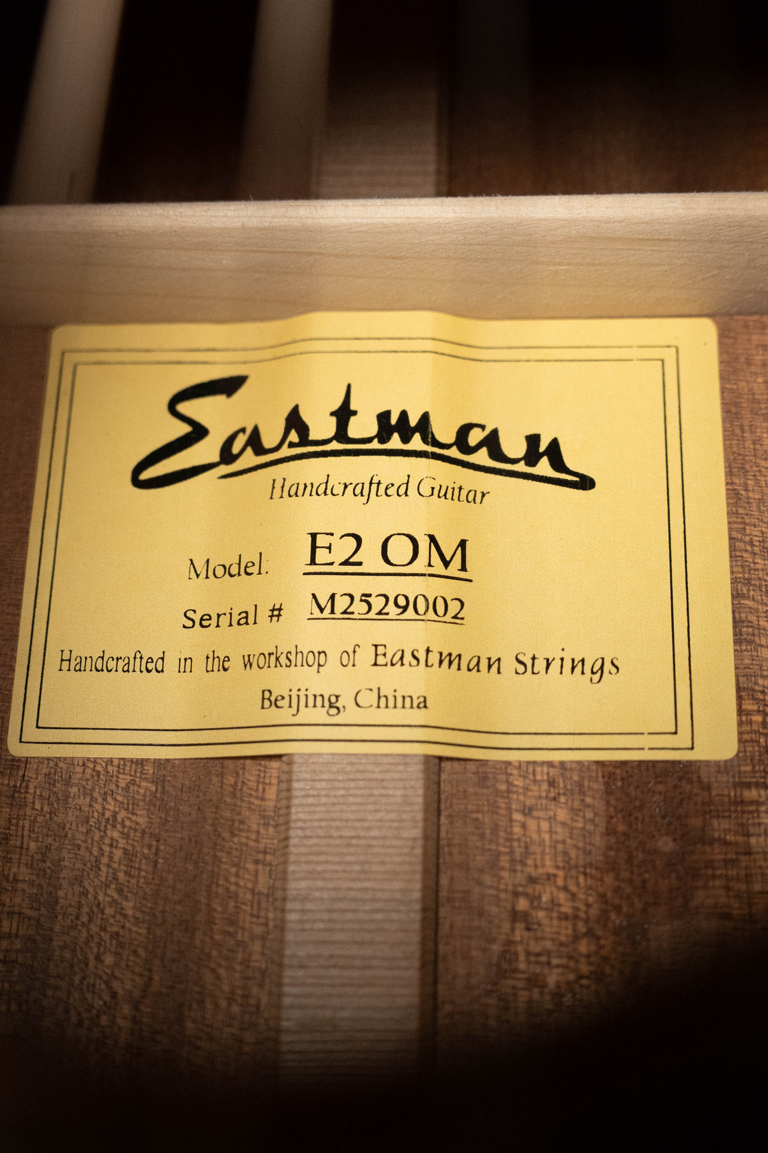 A yellow label inside the guitar reads: Eastman Guitars, Model: E2OM Cedar/Sapele Orchestra #9002. This handcrafted instrument features a solid cedar top and was made in Beijing, China by Eastman Guitars.