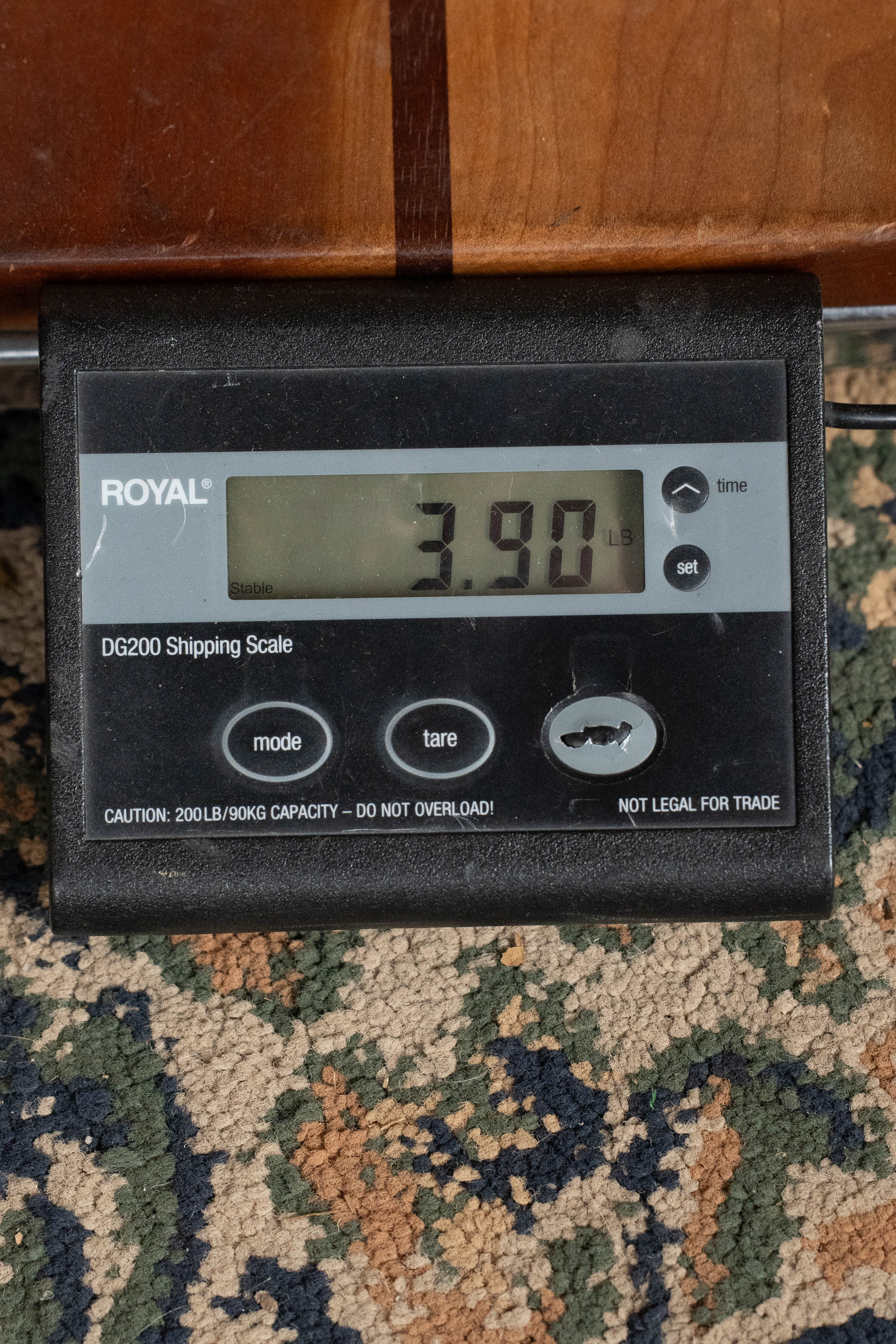 A ROYAL DG200 digital shipping scale on a patterned carpet shows 3.90 lbs beside an Eastman Guitars E2OM Cedar/Sapele Orchestra Model Acoustic Guitar #9002, highlighting its solid cedar top and fine craftsmanship.