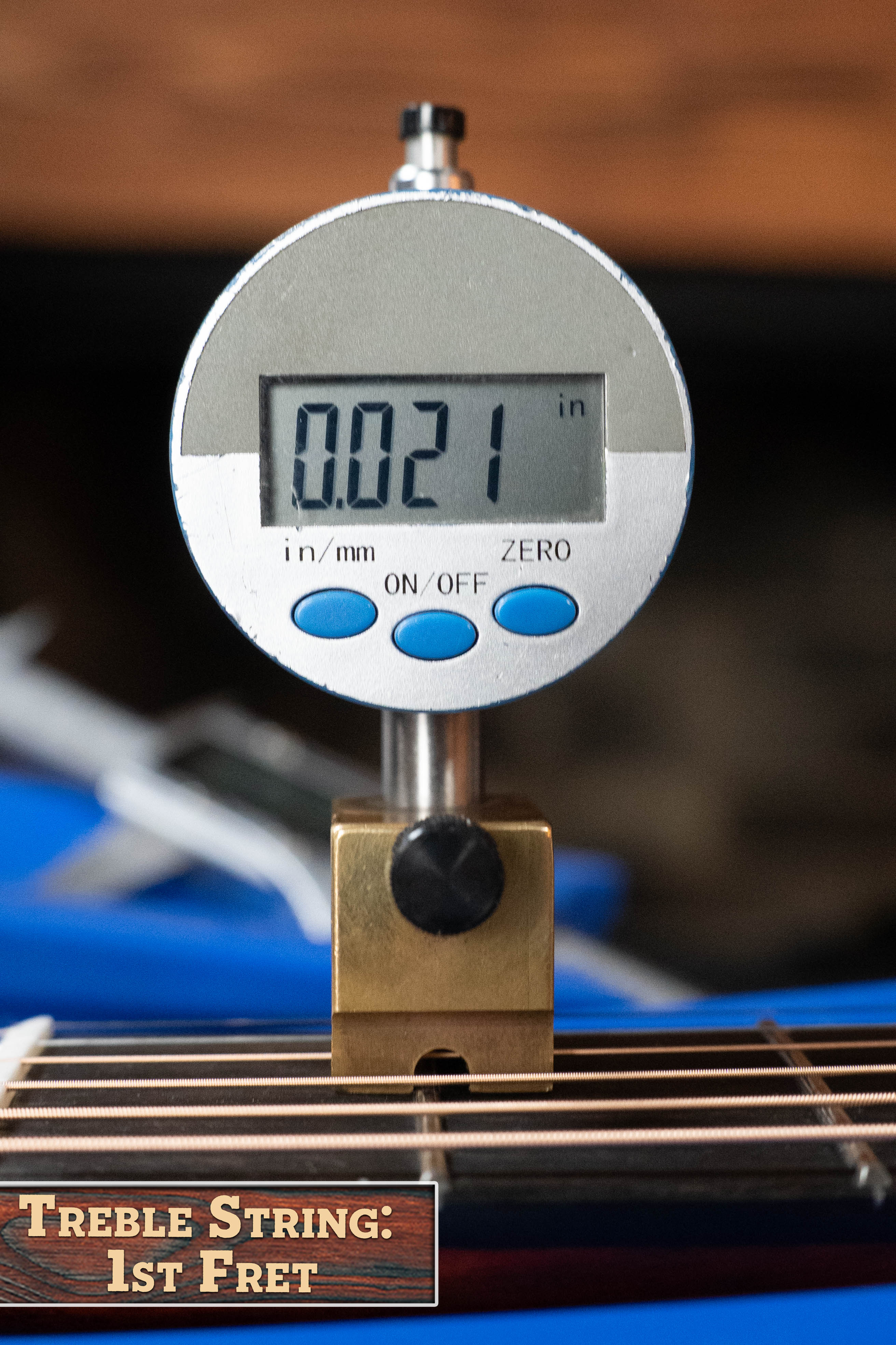 A digital gauge shows 0.021 inches as it measures the treble string height at the 1st fret of the Eastman Guitars E2OM Cedar/Sapele Orchestra Model Acoustic Guitar #9002. The label reads: Treble String: 1st Fret.