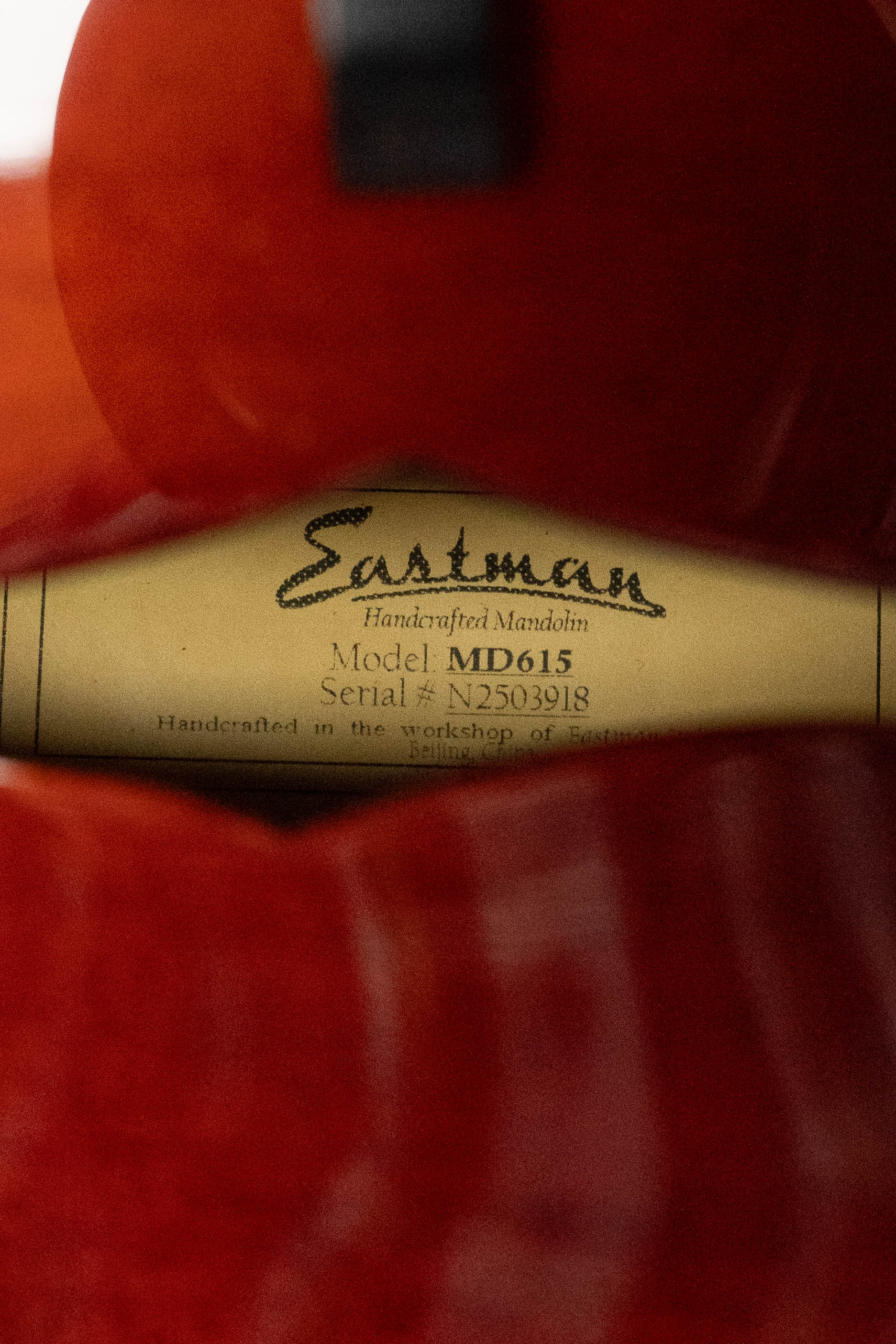 A close-up of a label inside a reddish-brown Eastman Guitars MD615 Spruce/Maple F-Style Mandolin w/K&K Pickup #3918, showing the model and serial numbers through the f-hole of this hand-carved instrument.