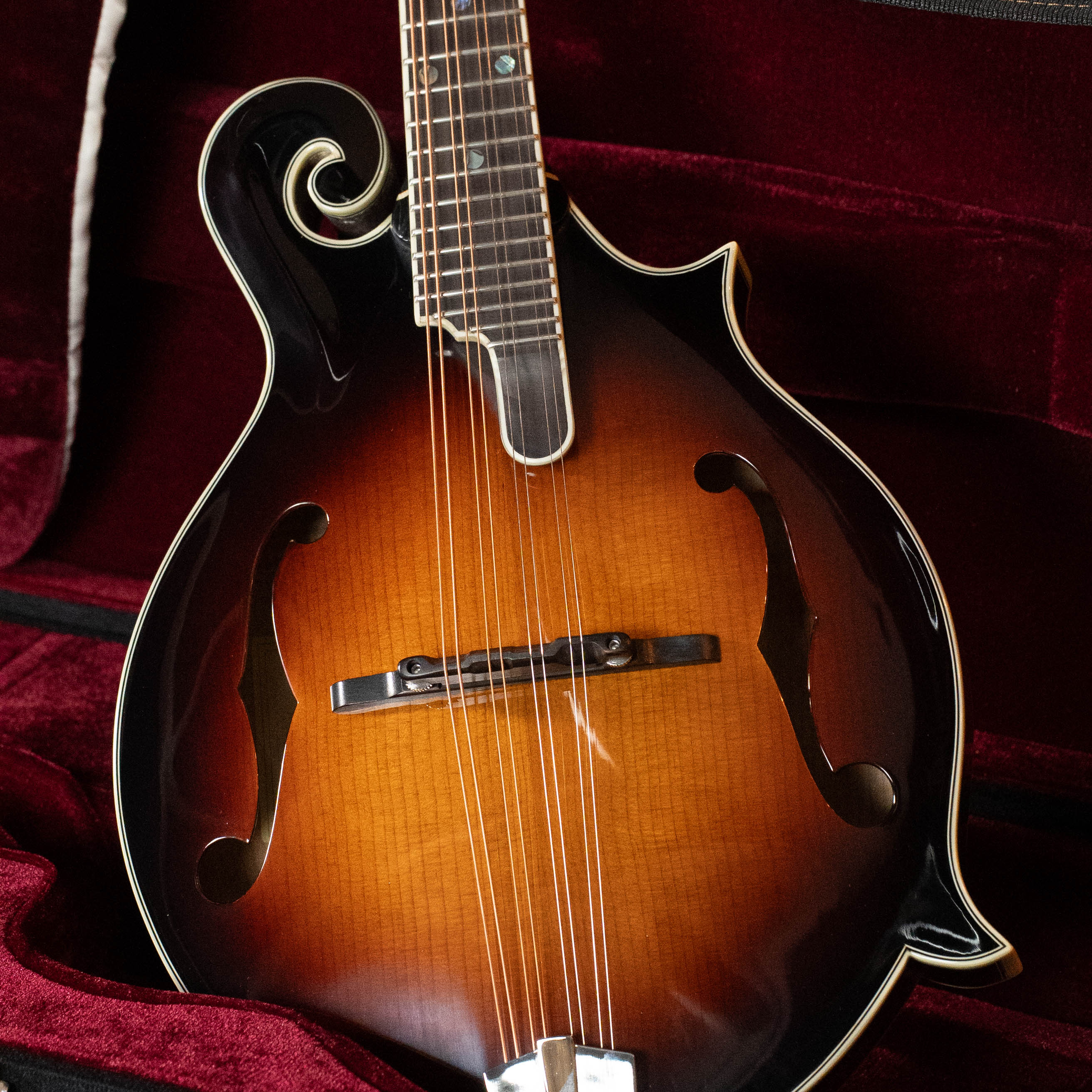 A close-up of an Eastman Guitars MD815-SB Adirondack/Flamed Maple Sunburst F-Style Mandolin #3356 with f-holes, glossy finish, and white binding, resting in a plush red velvet case.