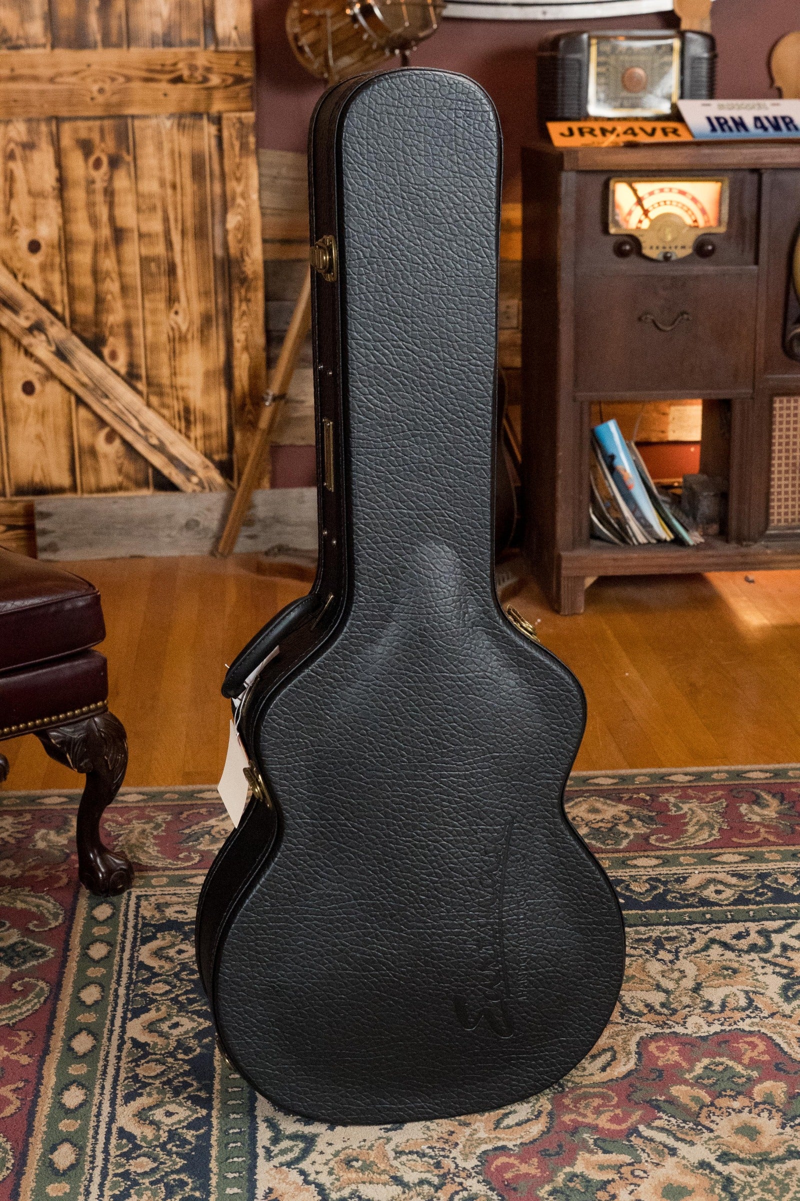 Black textured hard guitar case standing upright on patterned rug in rustic room setting. - Eastman AC722CE-DF European Spruce/Rosewood Dakota Fade Finish Grand Auditorium w/ LR Baggs Pickup #6872 - Default Title