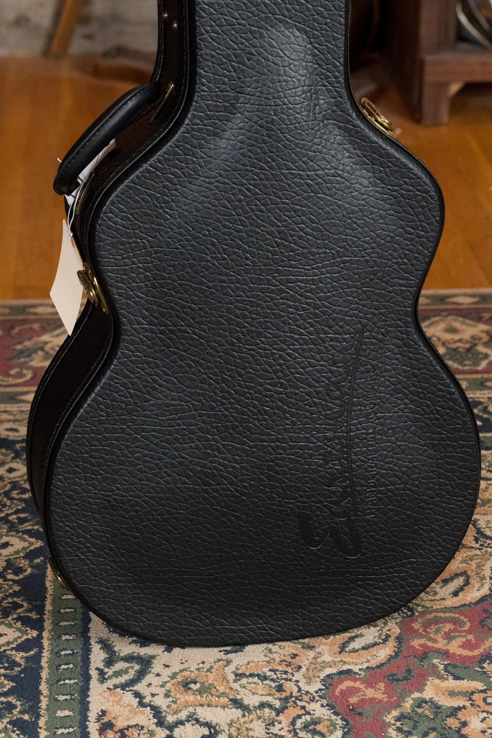 Black textured guitar case standing upright on a patterned rug with wooden furniture in the background. - Eastman AC722CE-DF European Spruce/Rosewood Dakota Fade Finish Grand Auditorium w/ LR Baggs Pickup #6872 - Default Title