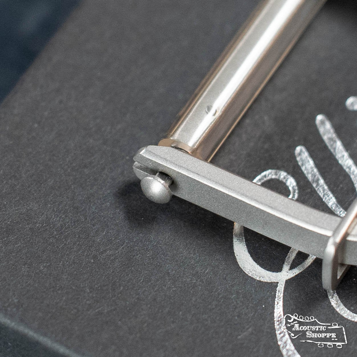 Close-up of the Elliott B450I Integrity Banjo Capo by Elliott Capos on a black box with white cursive writing and an Acoustic Shoppe logo—showcasing this store’s commitment to premium acoustic instrument accessories.