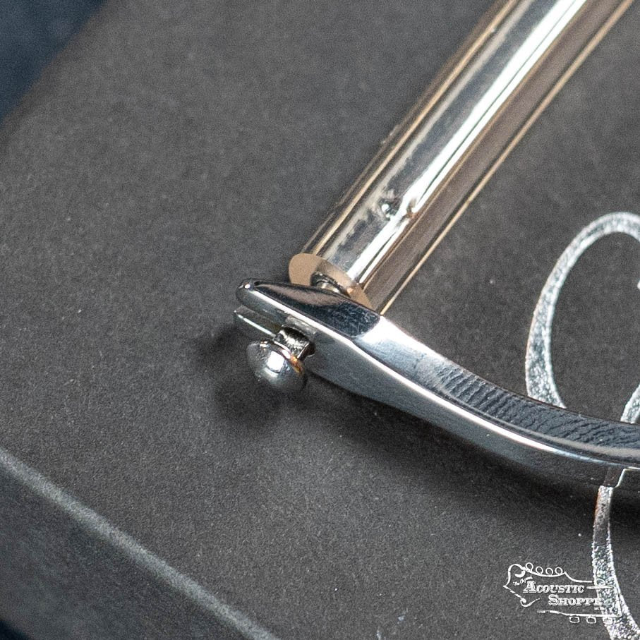 Close-up of an Elliott G78E Push Button Elite Capo (1 7/8, 16 radius) by Elliott Capos, resting on a dark box with stylized logo—ideal for boutique guitar fans or those wanting premium acoustic accessories.