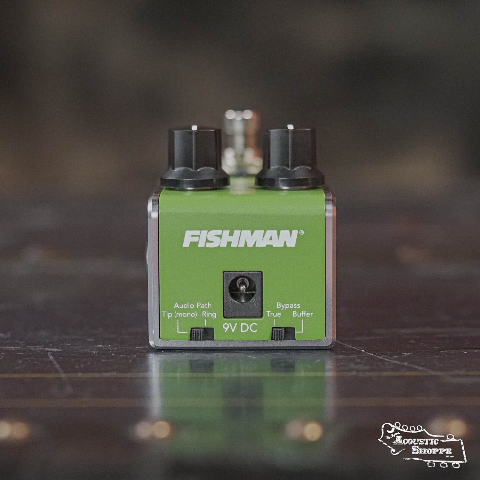 A Fishman AFX AcousticComp Mini Compressor PRO-AFX-CM2 pedal with input/output jacks and 9V DC port rests on a dark surface. The Acoustic Shoppe logo is in the lower right. This true bypass pedal delivers optimal signal clarity.