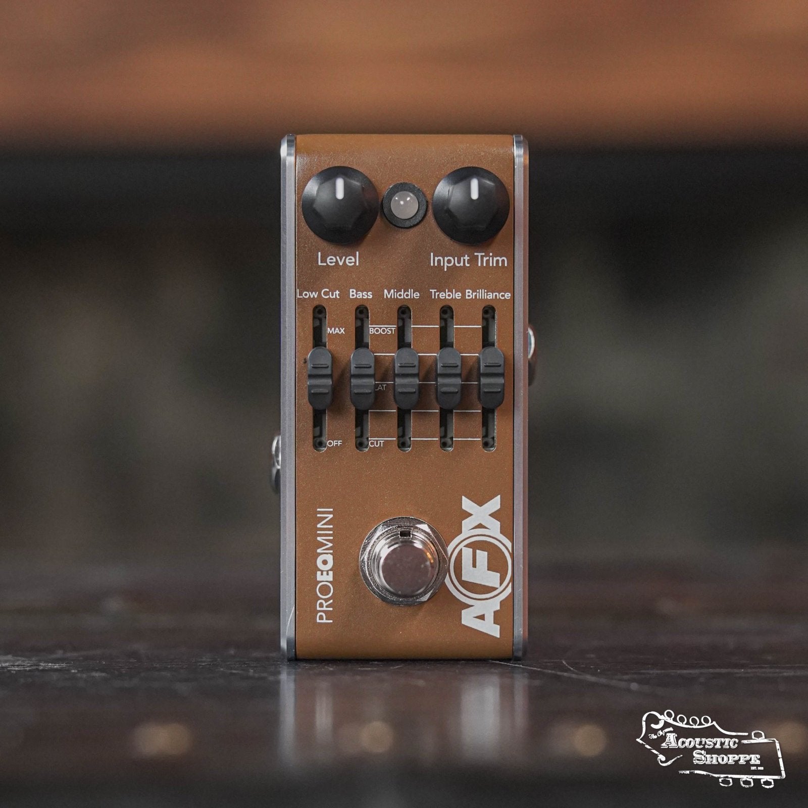 A brown Fishman AFX Pro EQ Mini Acoustic Preamp & EQ PRO-AFX-EQ2 pedal with Level and Input Trim knobs, five EQ sliders (Low Cut, Bass, Middle, Treble, Brilliance), and a silver footswitch. The Acoustic Shoppe logo is visible in the corner.