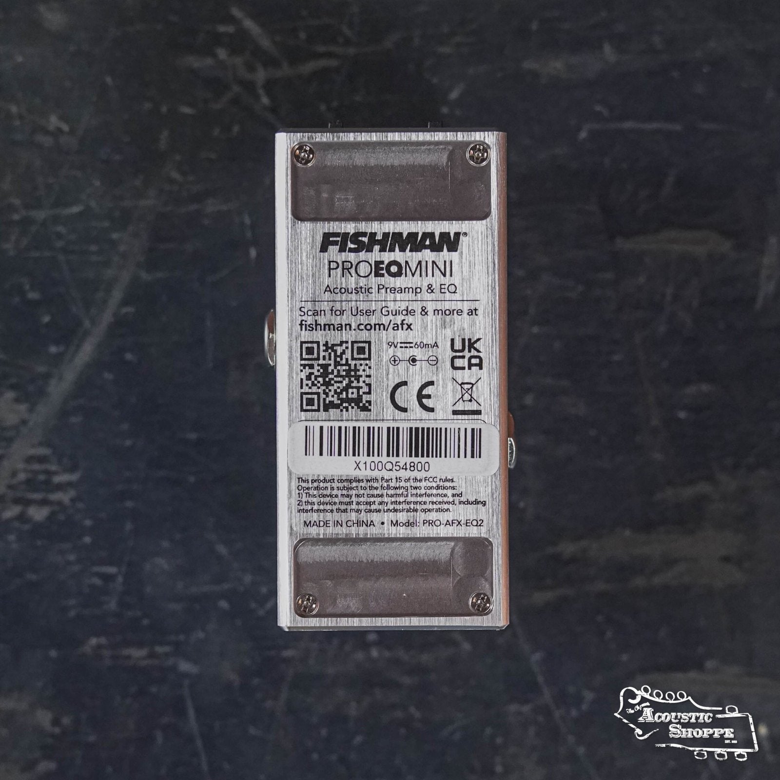 Rectangular Fishman AFX Pro EQ Mini Acoustic Preamp & EQ PRO-AFX-EQ2 pedal shown from the back with product label, barcode, QR code, and certification logos—an essential preamp for acoustic players—on a dark textured surface.