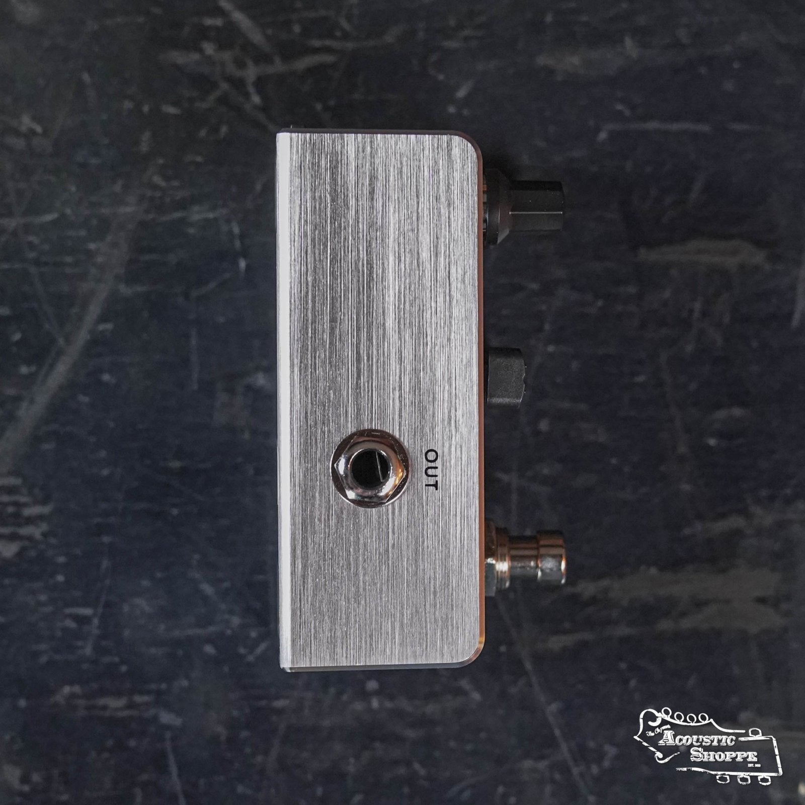 The Fishman AFX Pro EQ Mini Acoustic Preamp & EQ PRO-AFX-EQ2 is a brushed metal pedal with two black knobs, an OUT jack, and sits on a dark textured surface bearing the Acoustic Shoppe logo in the bottom right corner.