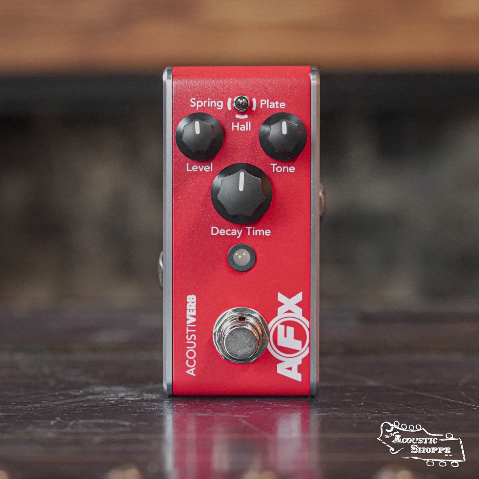 The Fishman AFX AcoustiVerb Mini Reverb Pedal PRO-AFX-RV2 is a red pedal with true bypass and three black knobs—Spring/Plate/Hall, Level/Tone, and Decay Time—designed for acoustic guitar reverb, shown on a wooden surface.