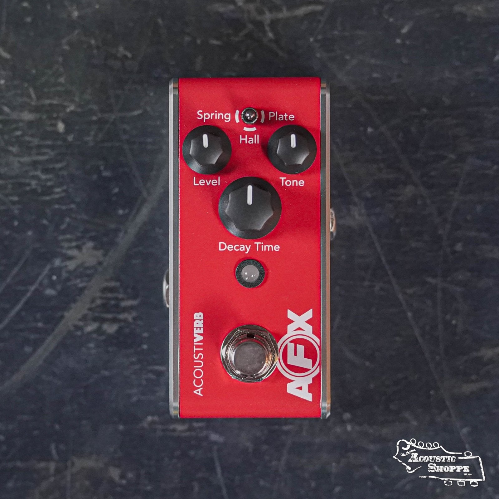 A Fishman AFX AcoustiVerb Mini Reverb Pedal PRO-AFX-RV2 in red, with black and white knobs labeled Spring/Plate/Hall, Level, Tone, and Decay Time, sits on a dark surface. True bypass; ideal for acoustic guitar. The Acoustic Shoppe logo is visible.