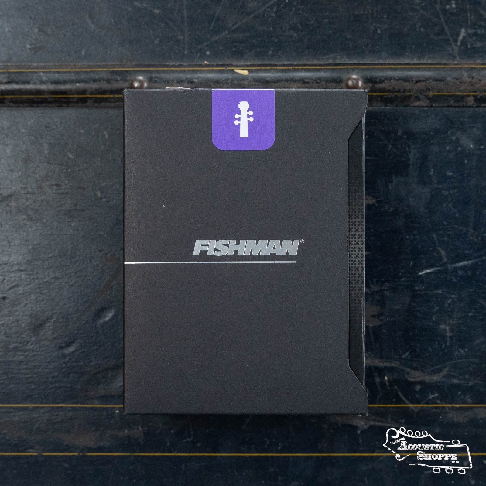 A black Fishman BP-100 Upright Bass Pickup (PRO-BP1-00B) box with a purple guitar headstock icon sits on a dark, worn surface. The FISHMAN logo is centered and Acoustic Shoppe branding appears in the lower right—ideal for upright bass players.