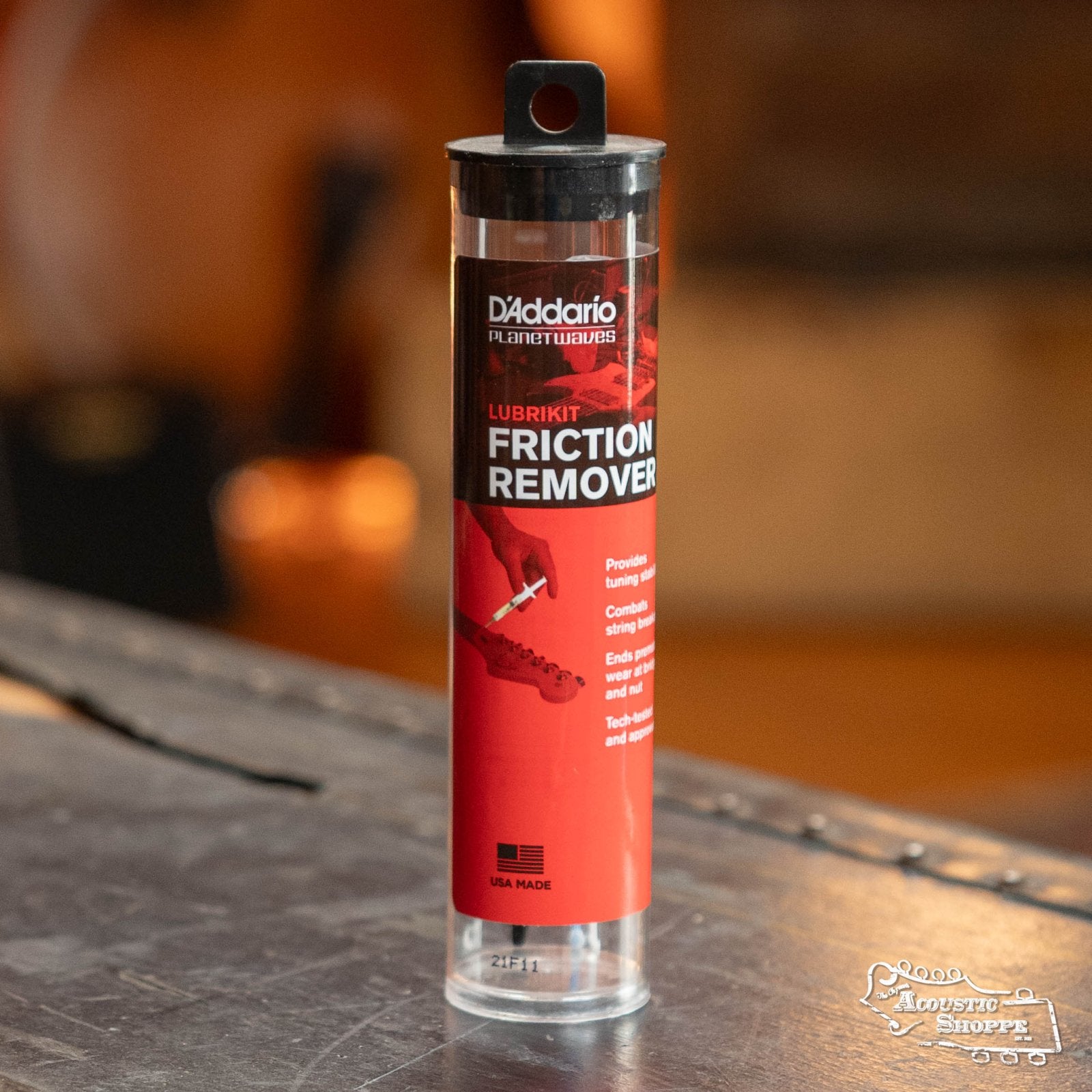 A DAddario PW-LBK-01 LubriKit Friction Remover cylindrical container, featuring a red and black label with product details and a guitar headstock illustration, is displayed on a table.