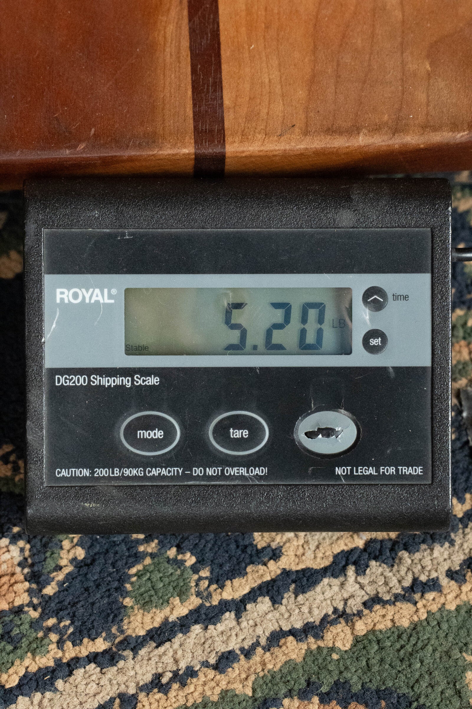 A digital shipping scale on patterned carpet displays 5.20 lbs, with a Furch Masters Choice Green SB Dc-SR AA Sitka/AA Indian Rosewood Dreadnought Cutaway Sunburst Guitar w/LR Baggs Pickup #0020 resting on top. The screen shows buttons and a caution label below.
