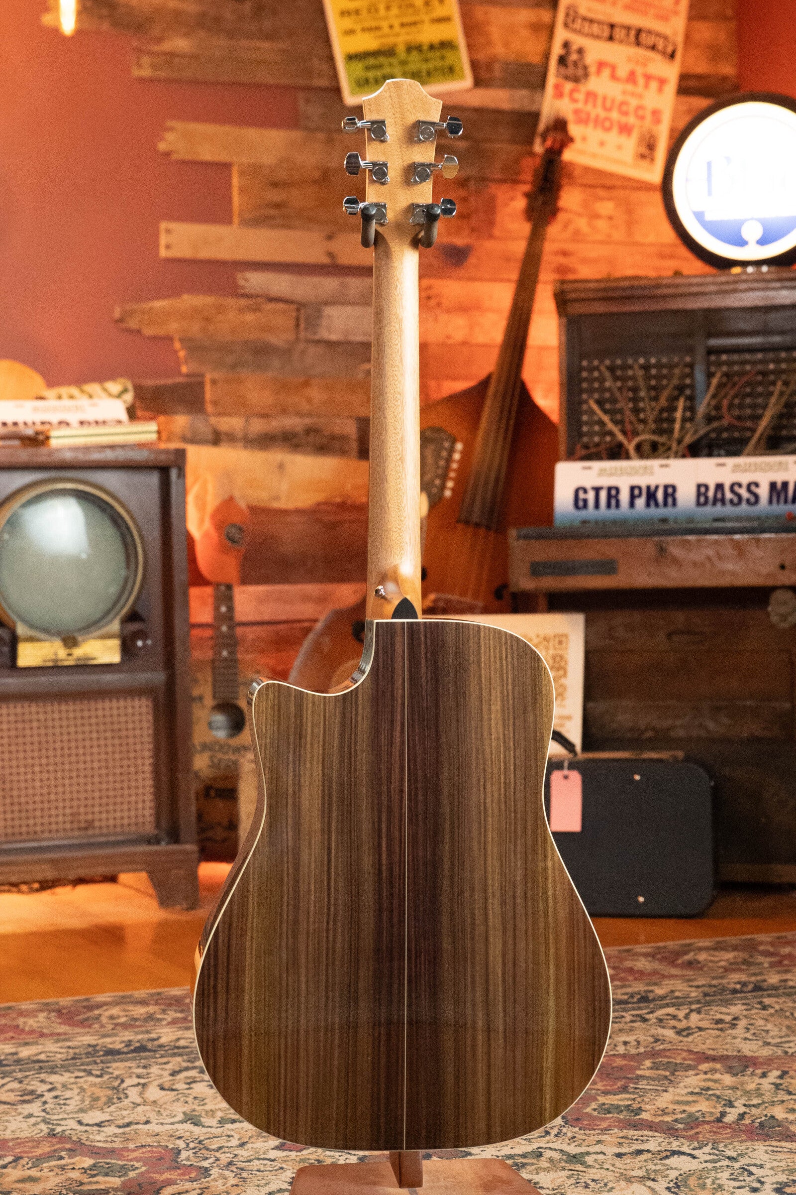 The Furch Masters Choice Green SB Dc-SR AA Sitka/AA Indian Rosewood Dreadnought Cutaway Sunburst Guitar w/LR Baggs Pickup #0020 is displayed from the back in a vintage room with wood-paneled walls, an old TV, music signs, and instruments.