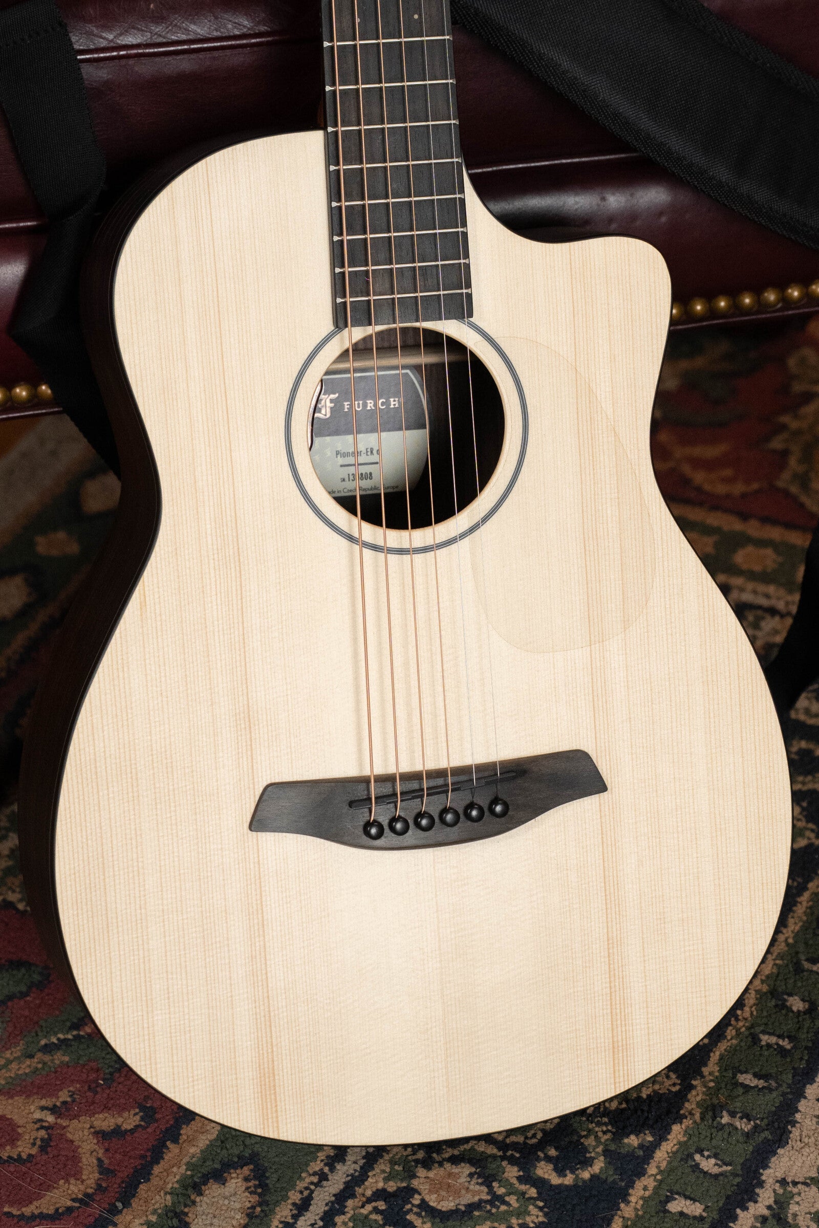 A close-up of the Furch Pioneer-ER VTC Engelmann Spruce/Indian Rosewood Cutaway Travel Guitar with Soundport Boosters & VTC Pickup, showing strings, soundhole, bridge, and part of the neck on a patterned rug.