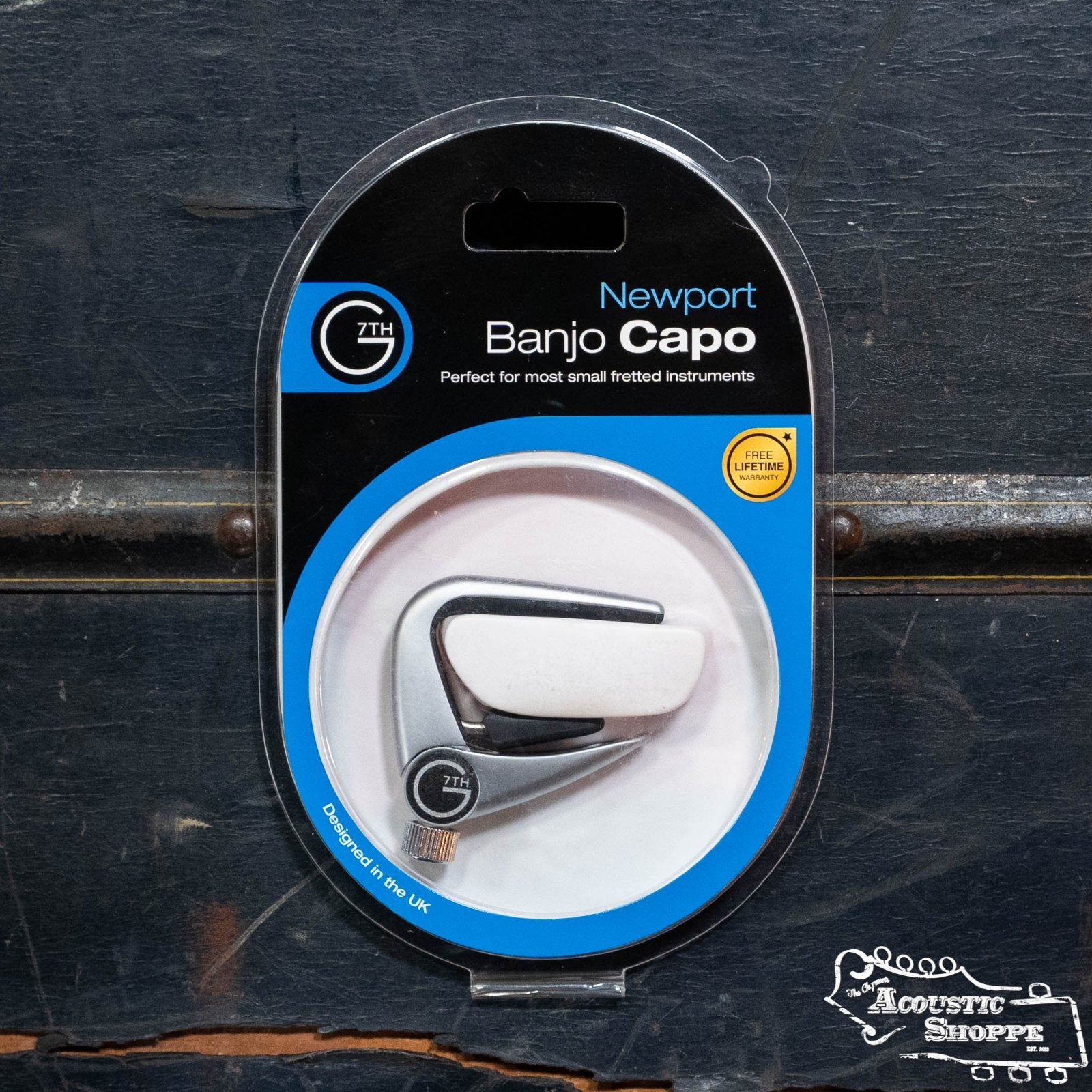 A packaged G7th Banjo Newport Capo (G7NPBU-U) is shown against a dark background, featuring "The Acoustic Shoppe" logo in the lower right corner.