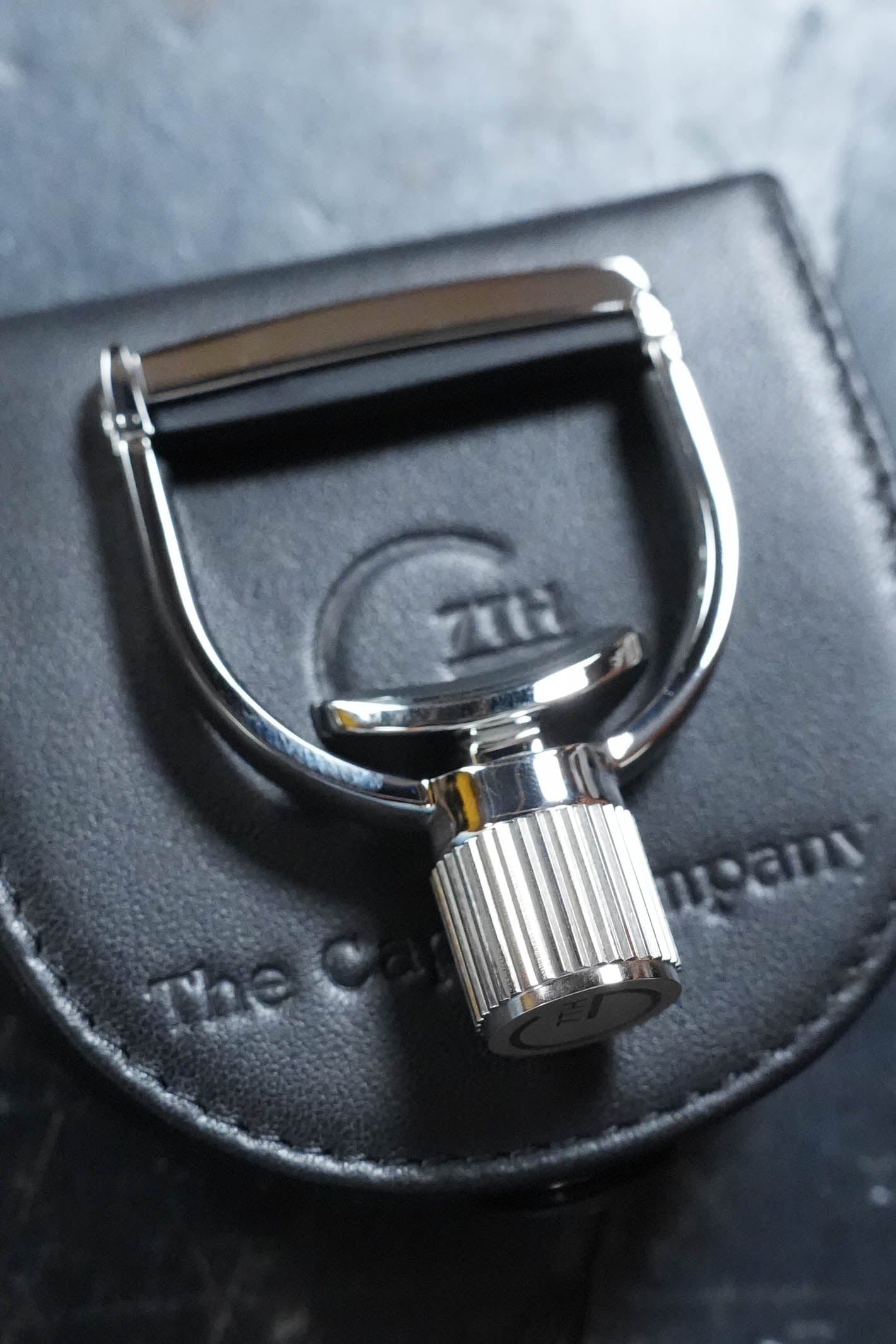 A shiny G7th Heritage Banjo Capo S1 Standard Neck Width by The Acoustic Shoppe rests on a black leather pouch embossed with The Capo Company and 7th logo, its textured knob visible in the foreground.